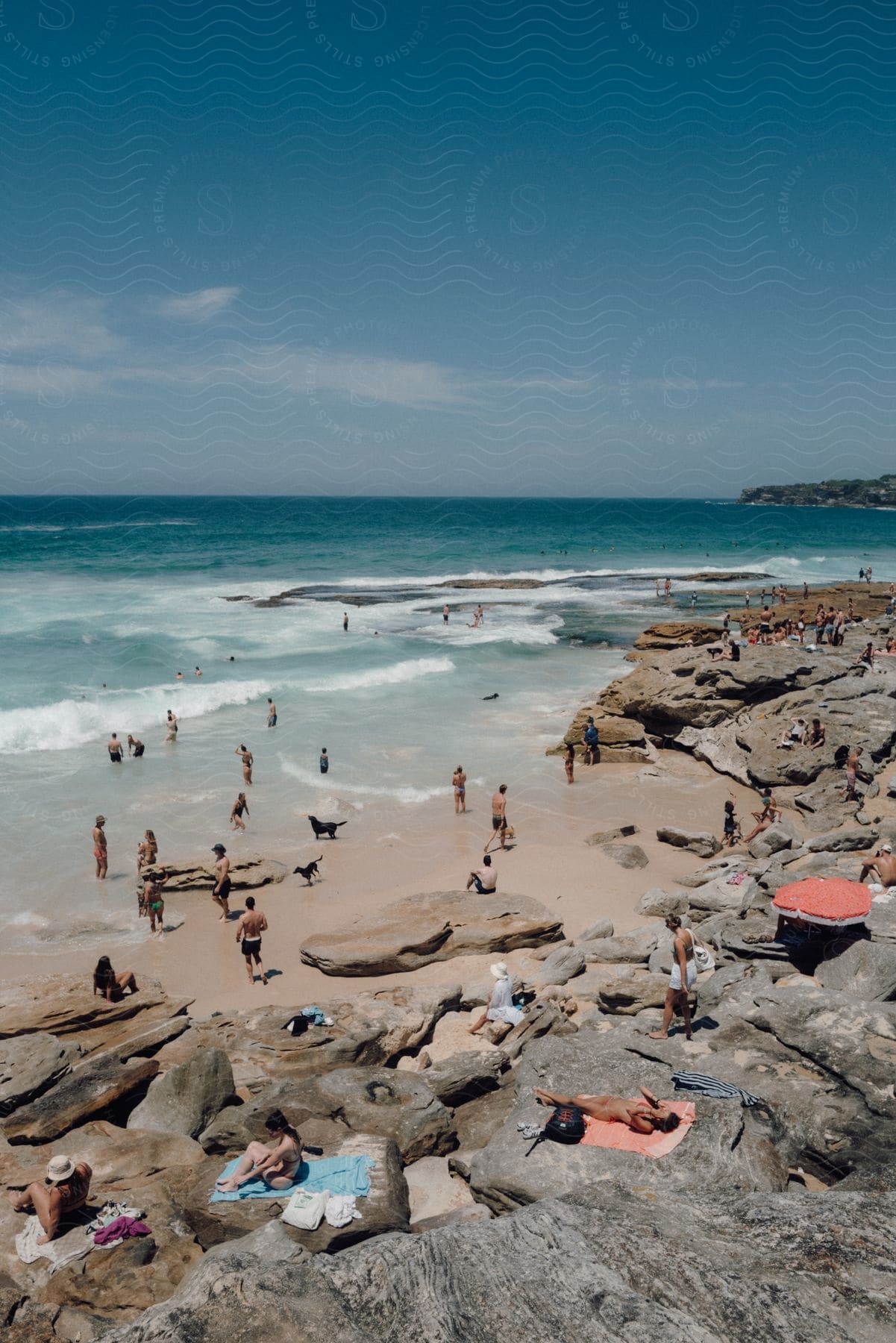 Many people on rocks along the coast and relaxing on a crowded beach and swimming in the water