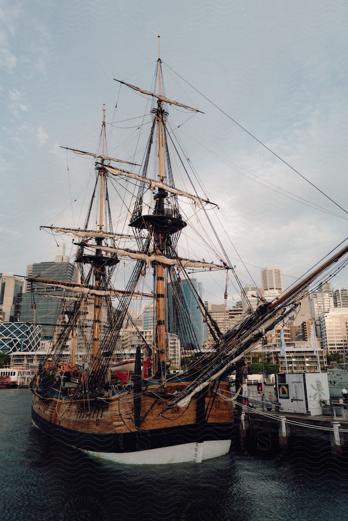 Historic tall ship moored at a city waterfront with modern buildings in the background.