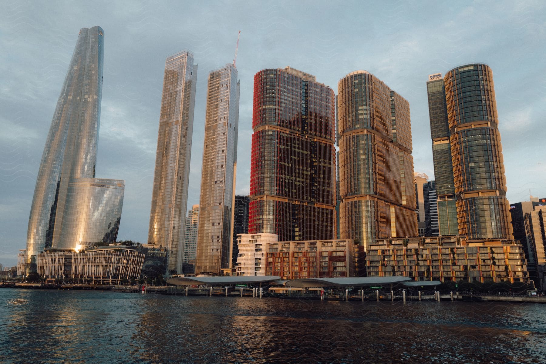 Modern city skyline with tall glass skyscrapers reflecting sunlight, seen from a waterfront perspective.