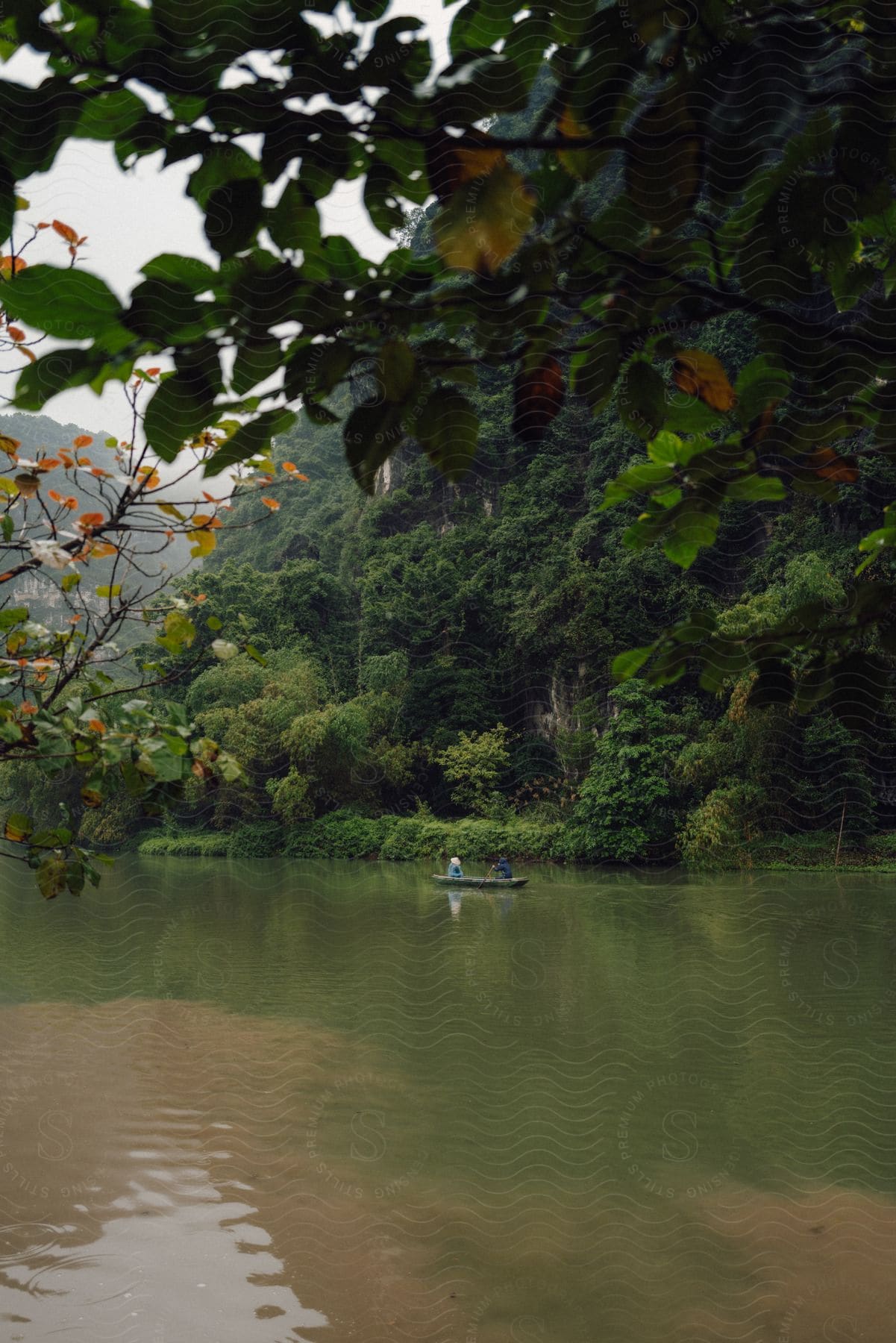 Two people in a canoe down a wide river with forested mountains around