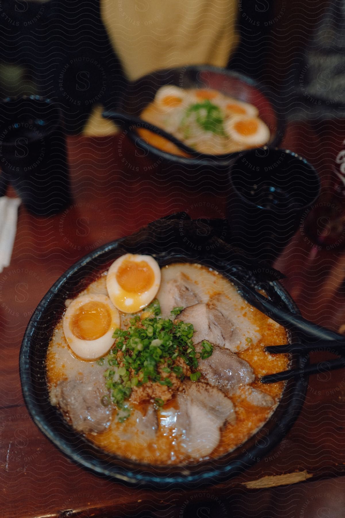 A steaming bowl of ramen with slices of pork, a halved hard-boiled egg, and chopped green onions sits on a wooden table.