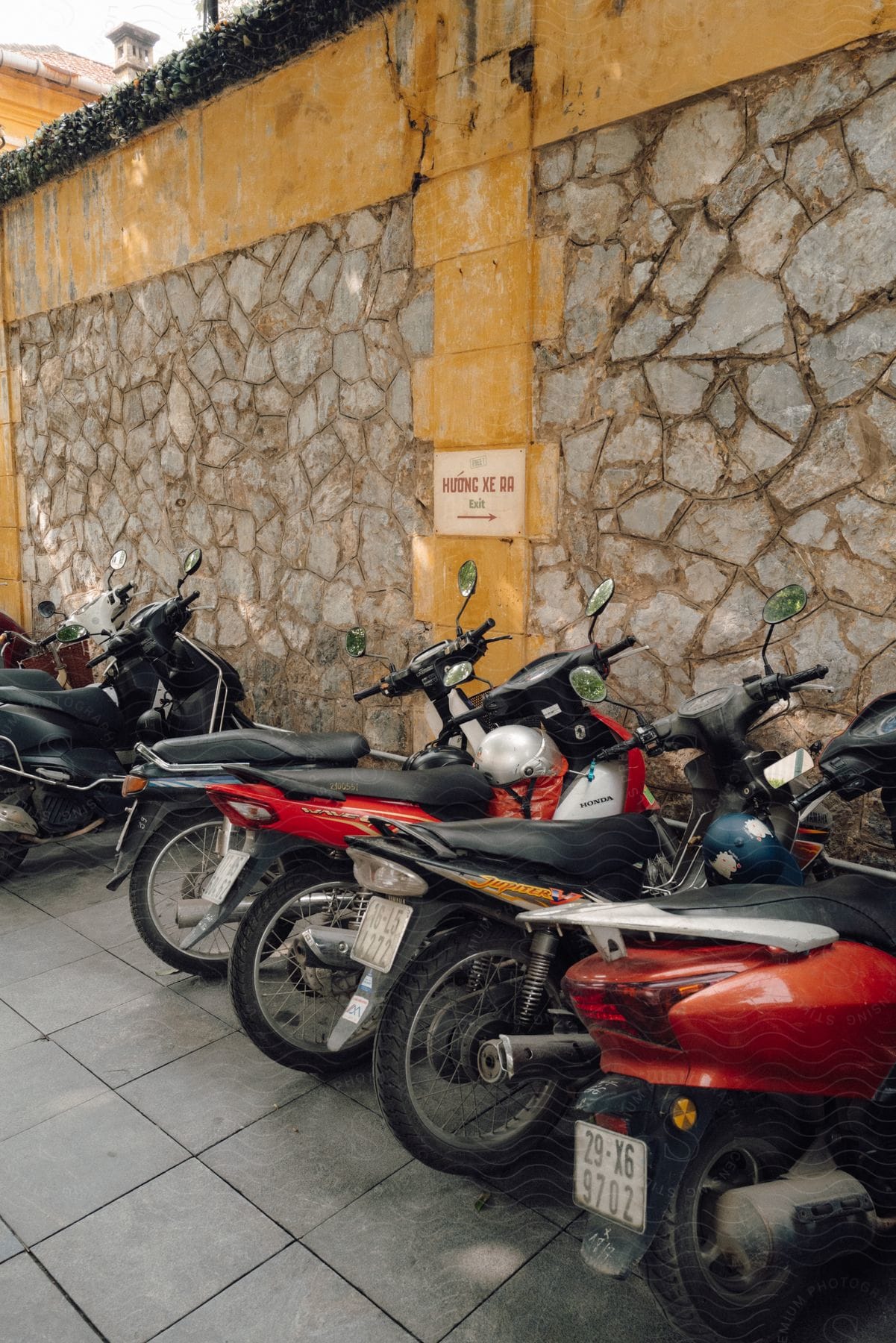 Motor scooters lined up along an old rocky wall.