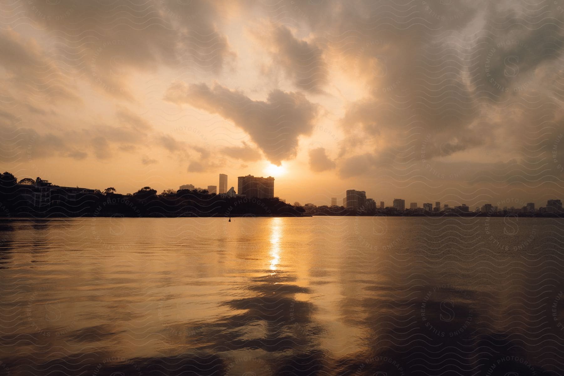 Landscape of a lake with a metropolis in the background with the orange sun in the horizon.