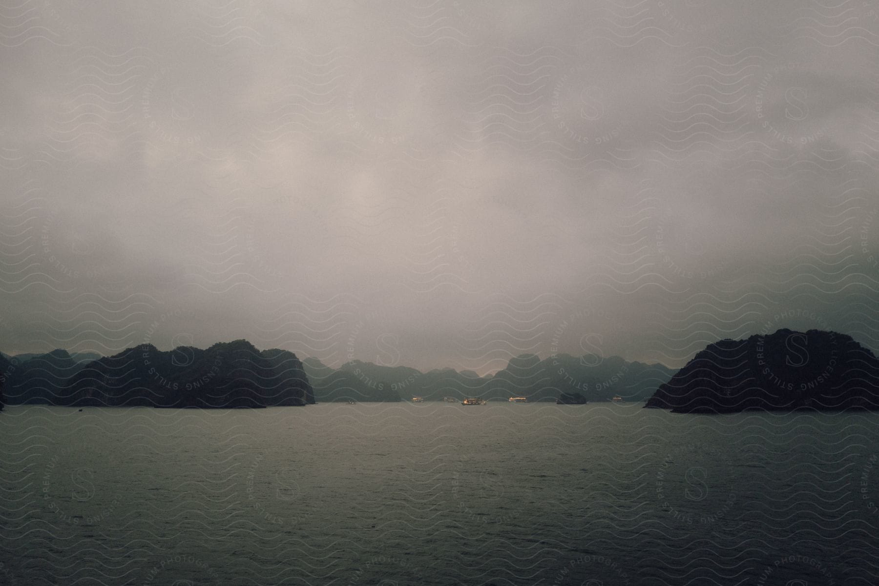 A serene, misty landscape with distant mountains and a few boats at dusk.