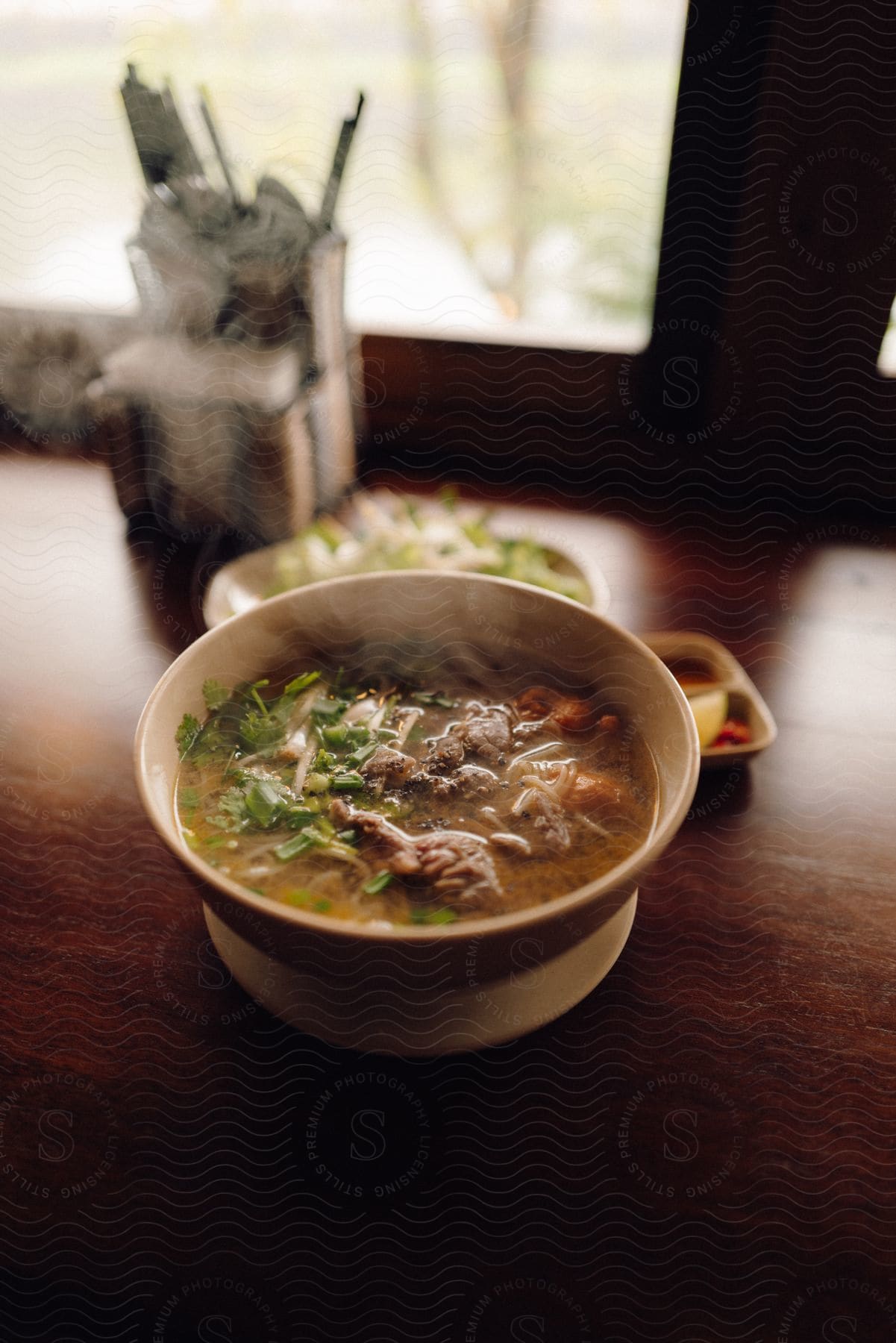 A bowl that is on a table and has a soup with meat and small crushed green leaves