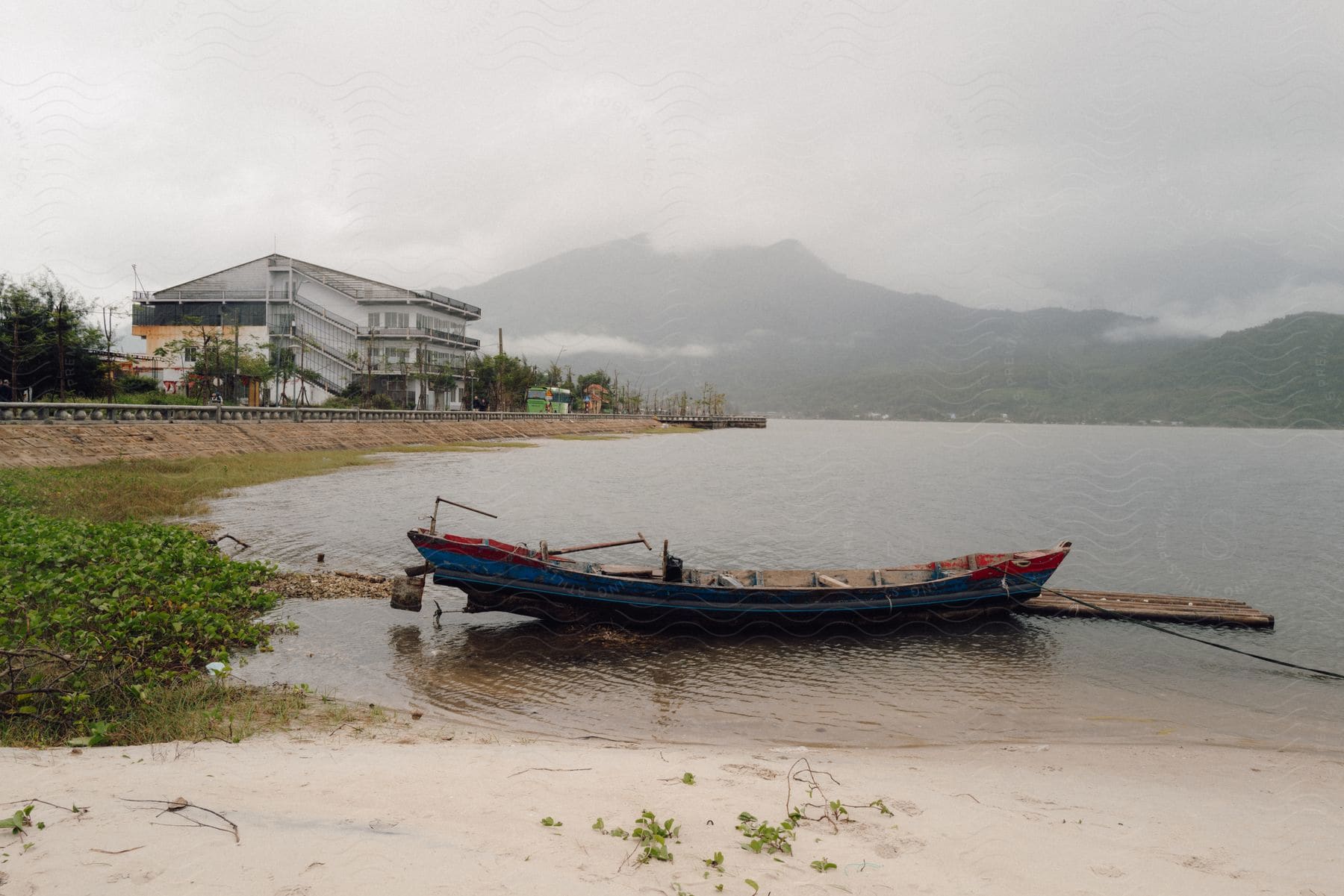 a small, wooden rowboat with blue paint peeling off, resting on the sandy shore of a calm lake.