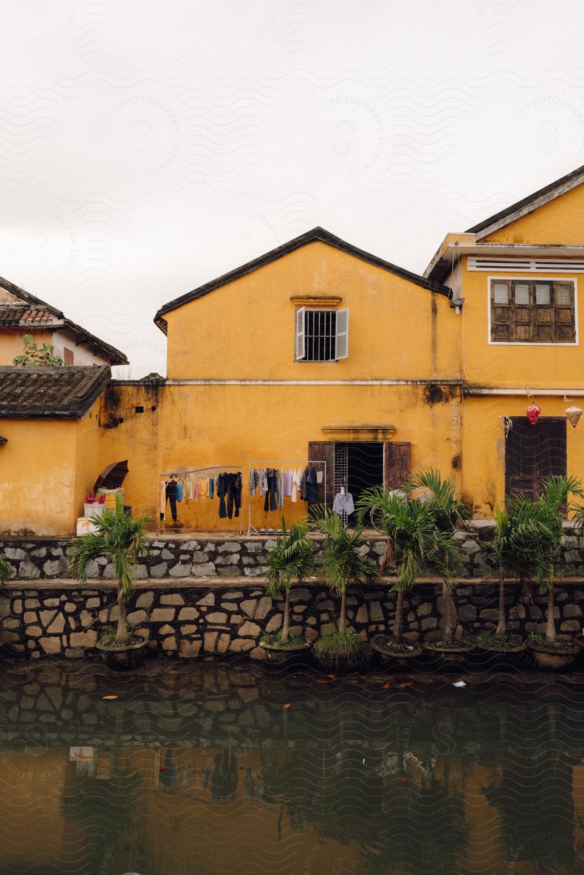 a yellow house with a red tiled roof next to a river, in the town of Hoi An, Vietnam.