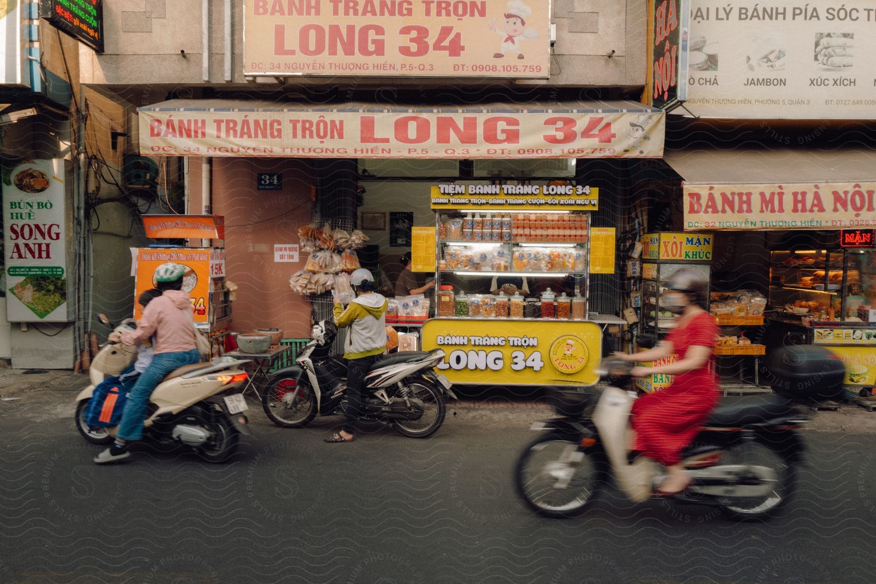 People ride motor bikes on a city street by food carts