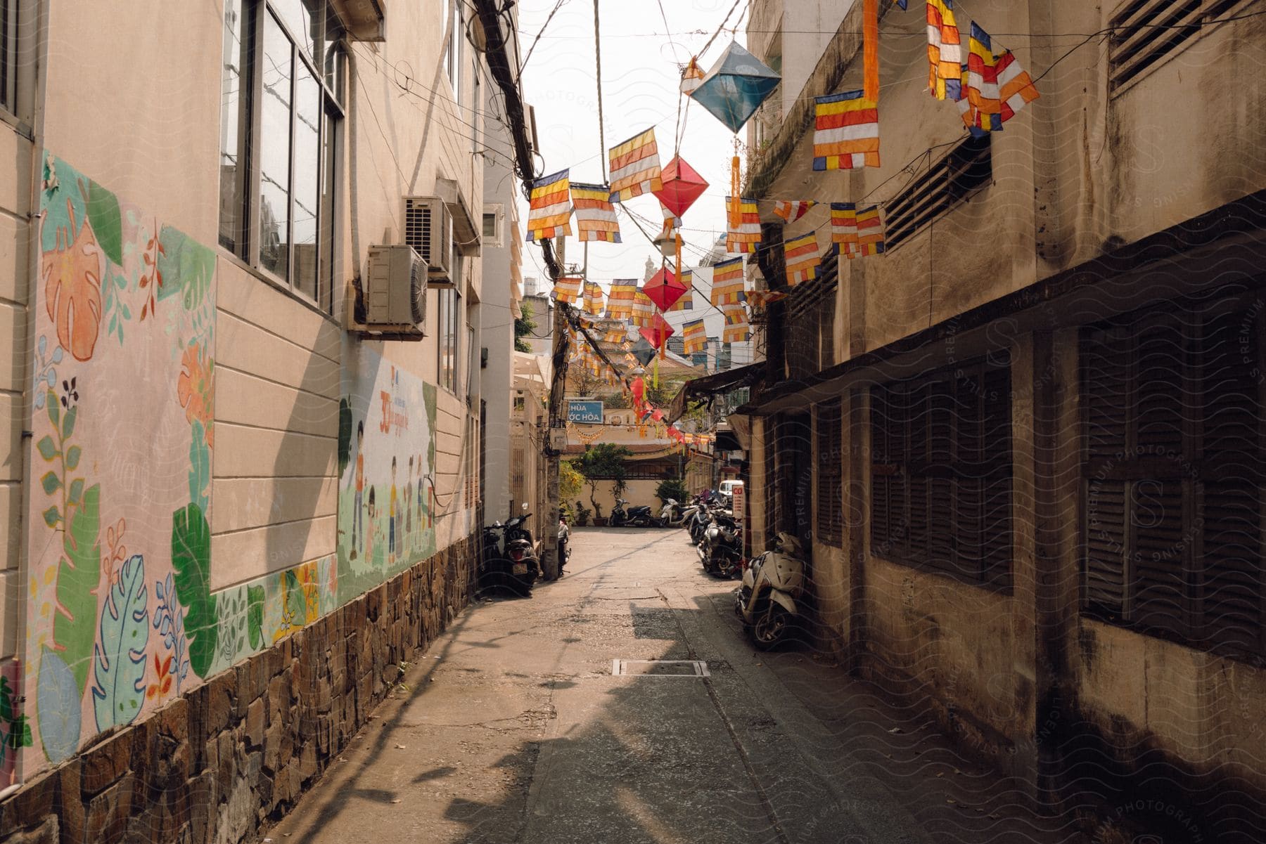 Motorbikes are parked in a neighborhood alley with colored flags strung overhead