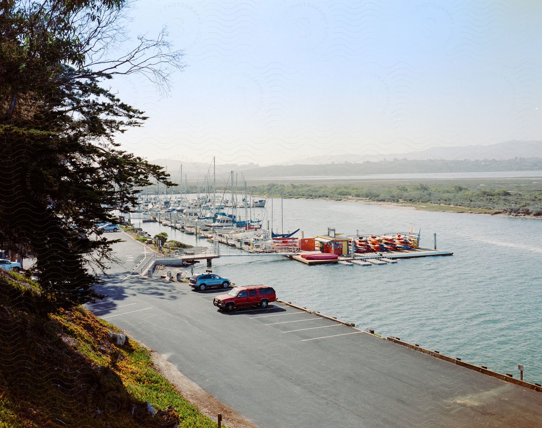 Overlooking a marina with rows of docked boats, a parking lot to the side with two vehicles, and hills in the distance.