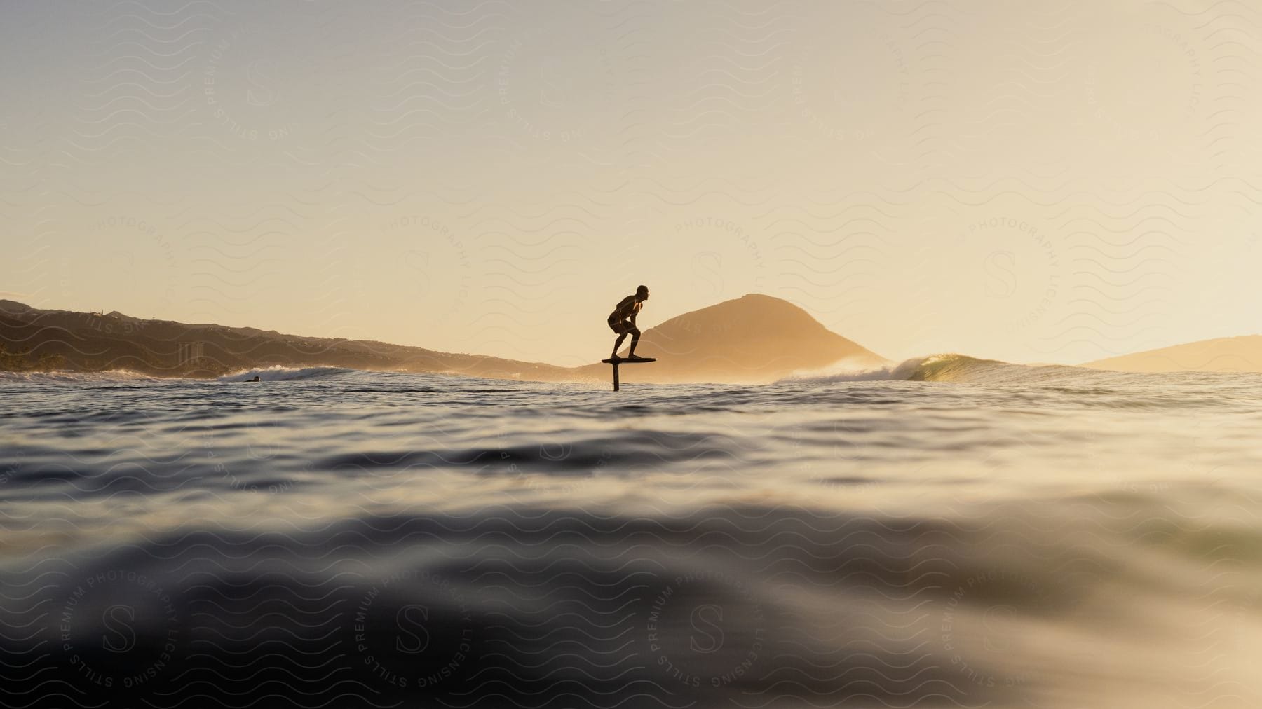 Man balances on flying surfboard while facing away from the shore.