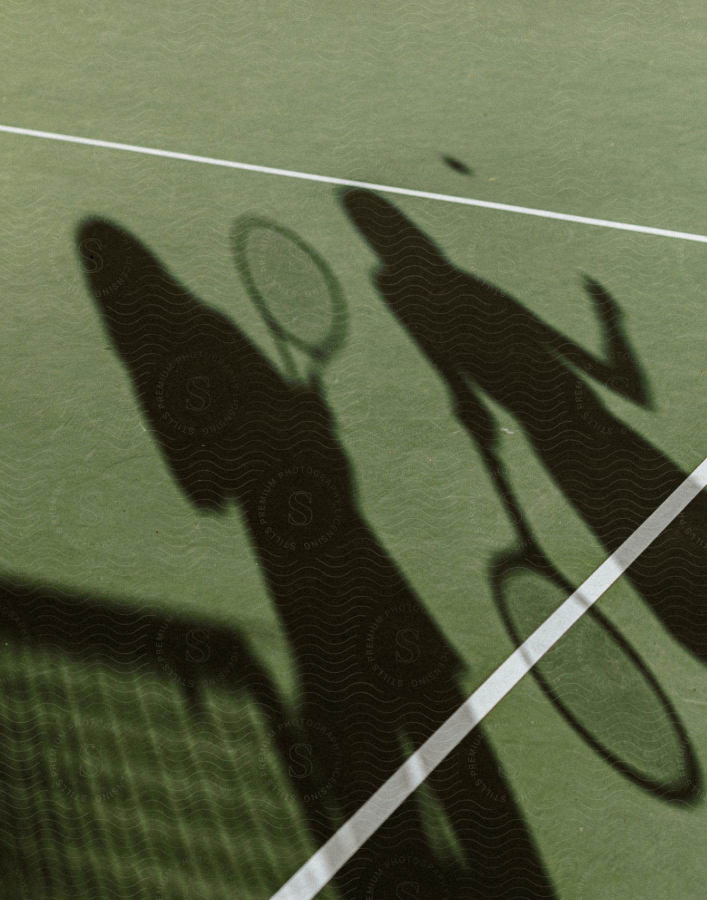 The silhouette of two people holding tennis rackets and a tennis ball in the air on a tennis court.