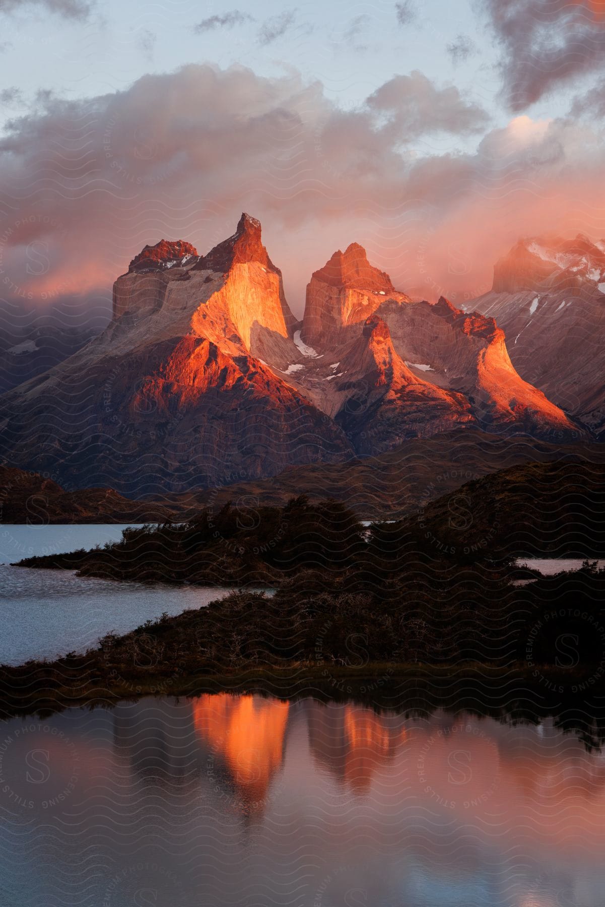 Sunlight shines on a steep mountain range next to a large lake at sunset.