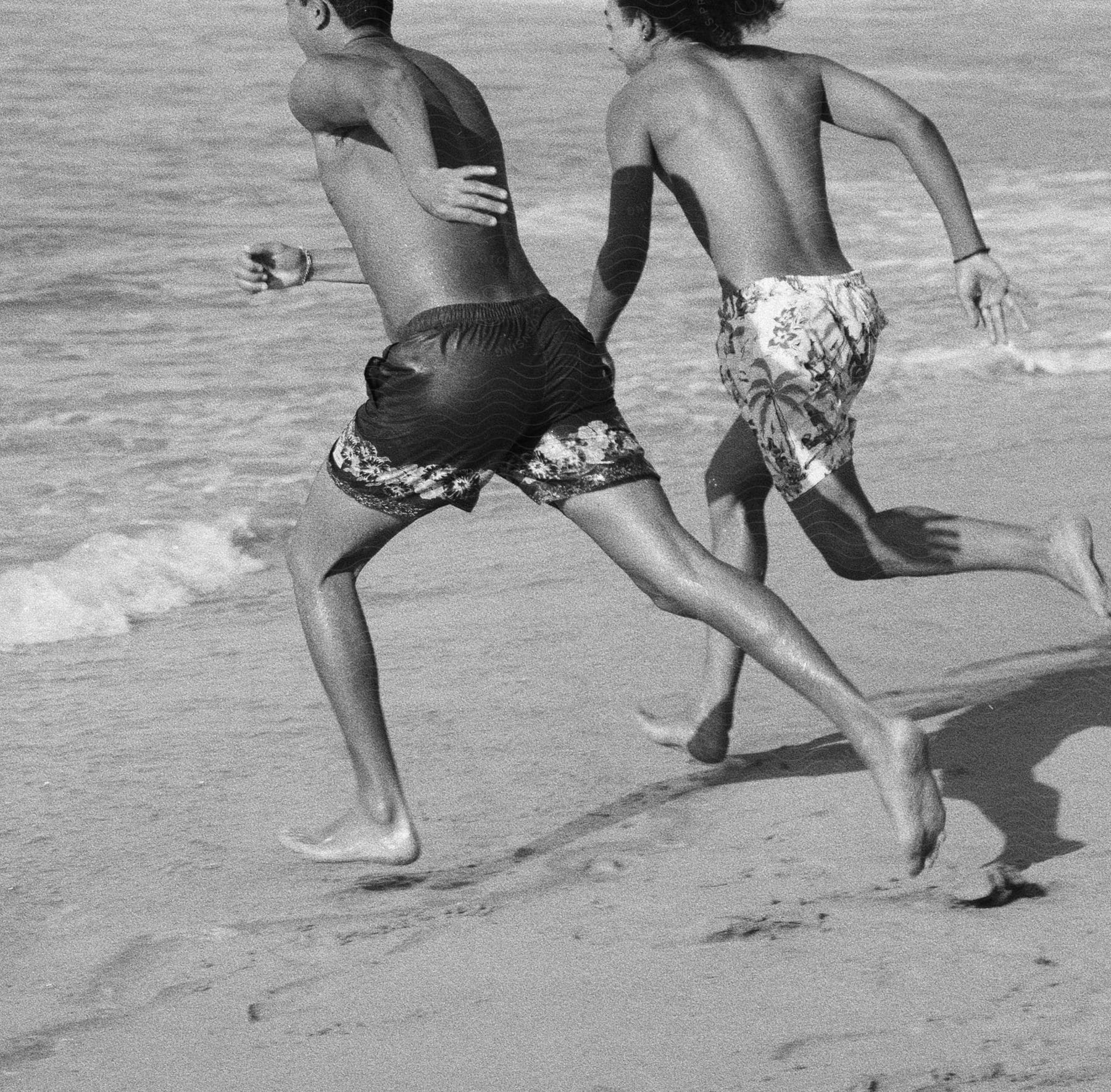 Black and white of two men running on the beach toward the ocean waves.