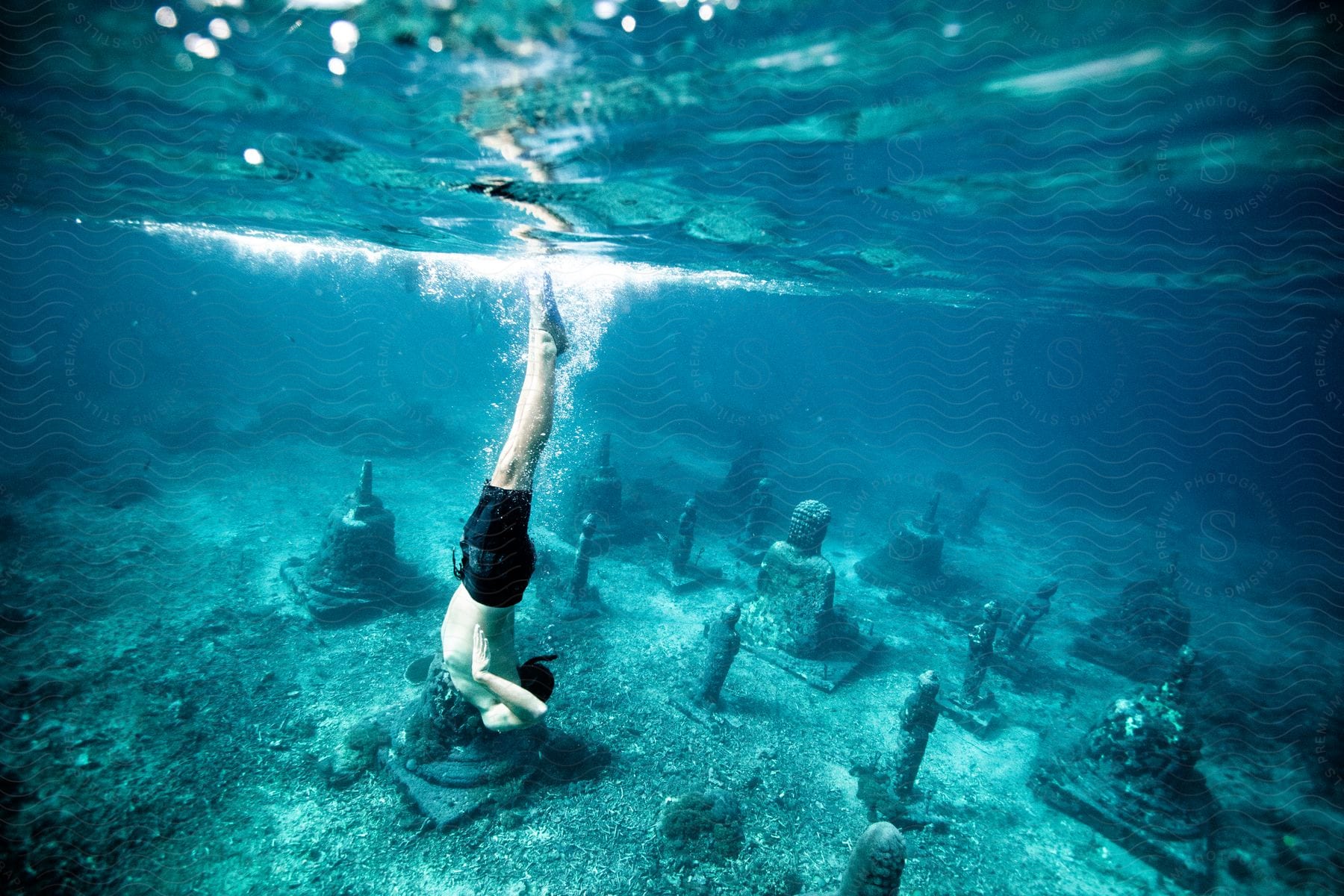 A person diving underwater where there are several statues at the bottom