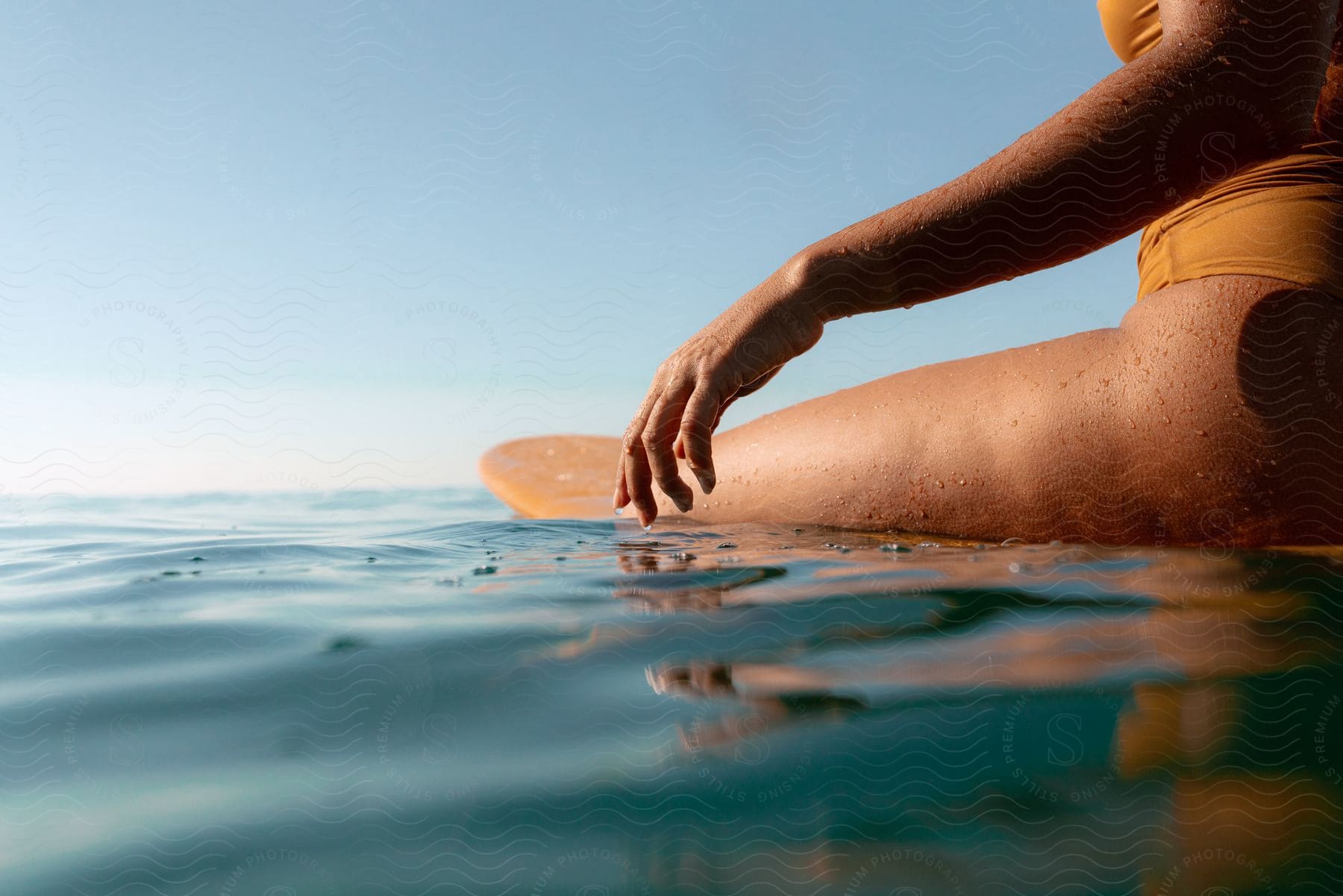A sun-kissed woman in a vibrant orange bikini gracefully rides the gentle swells of the ocean on her surfboard, her silhouette mirroring the serene horizon.