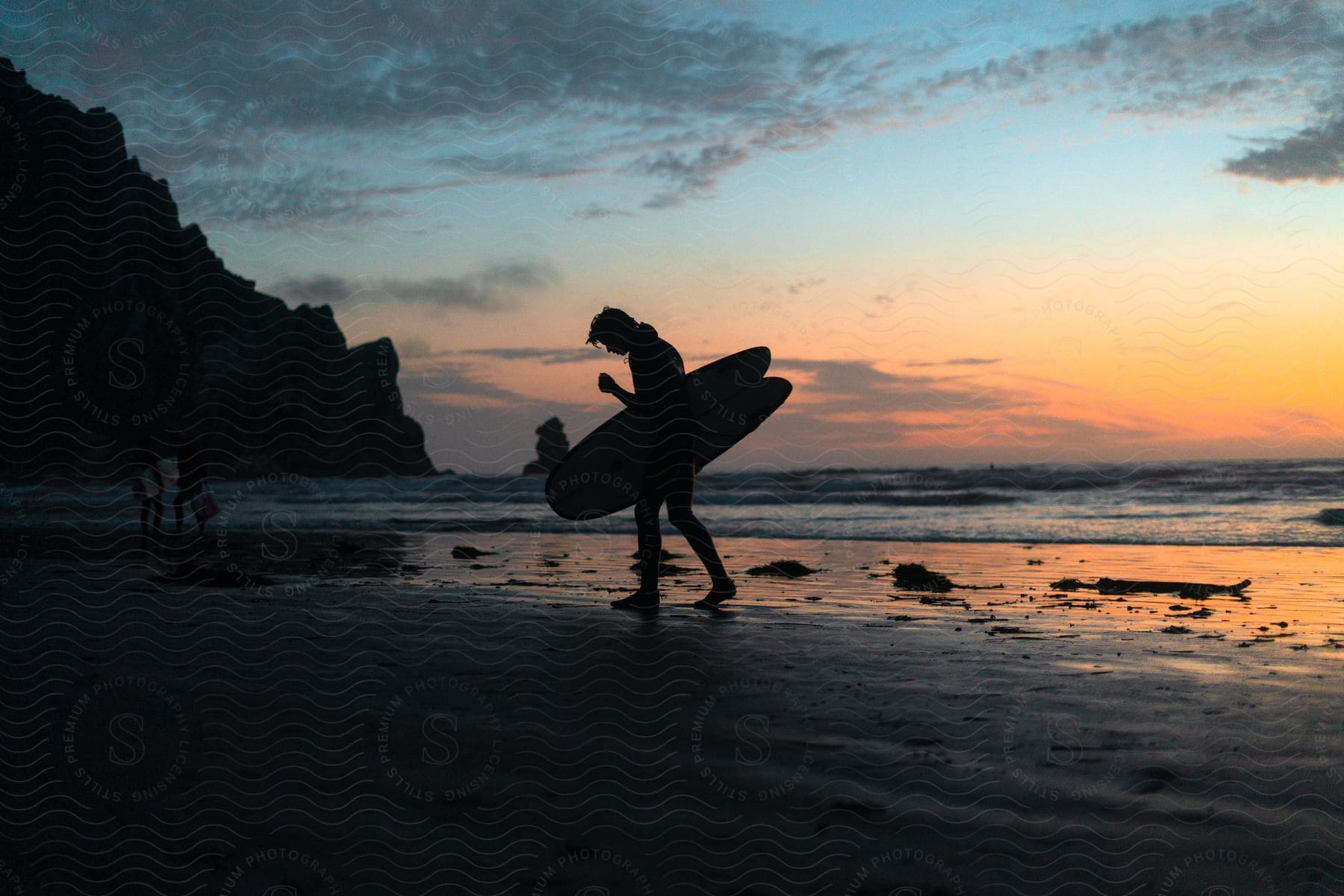 Surfer standing on beach holding a surfboard is silhouetted against red horizon during sunset.