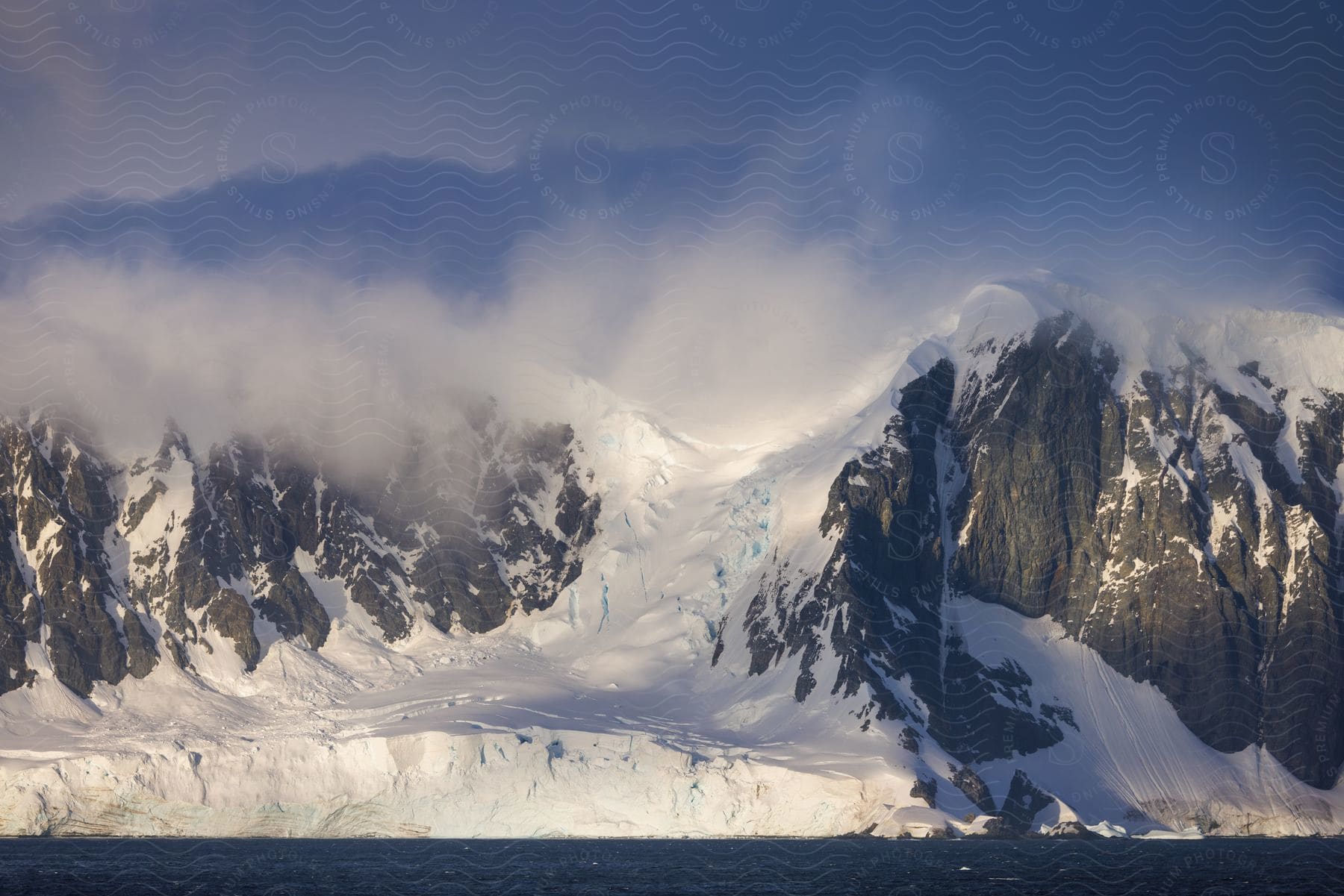 Snowy mountain range by the sea with cloudy sky