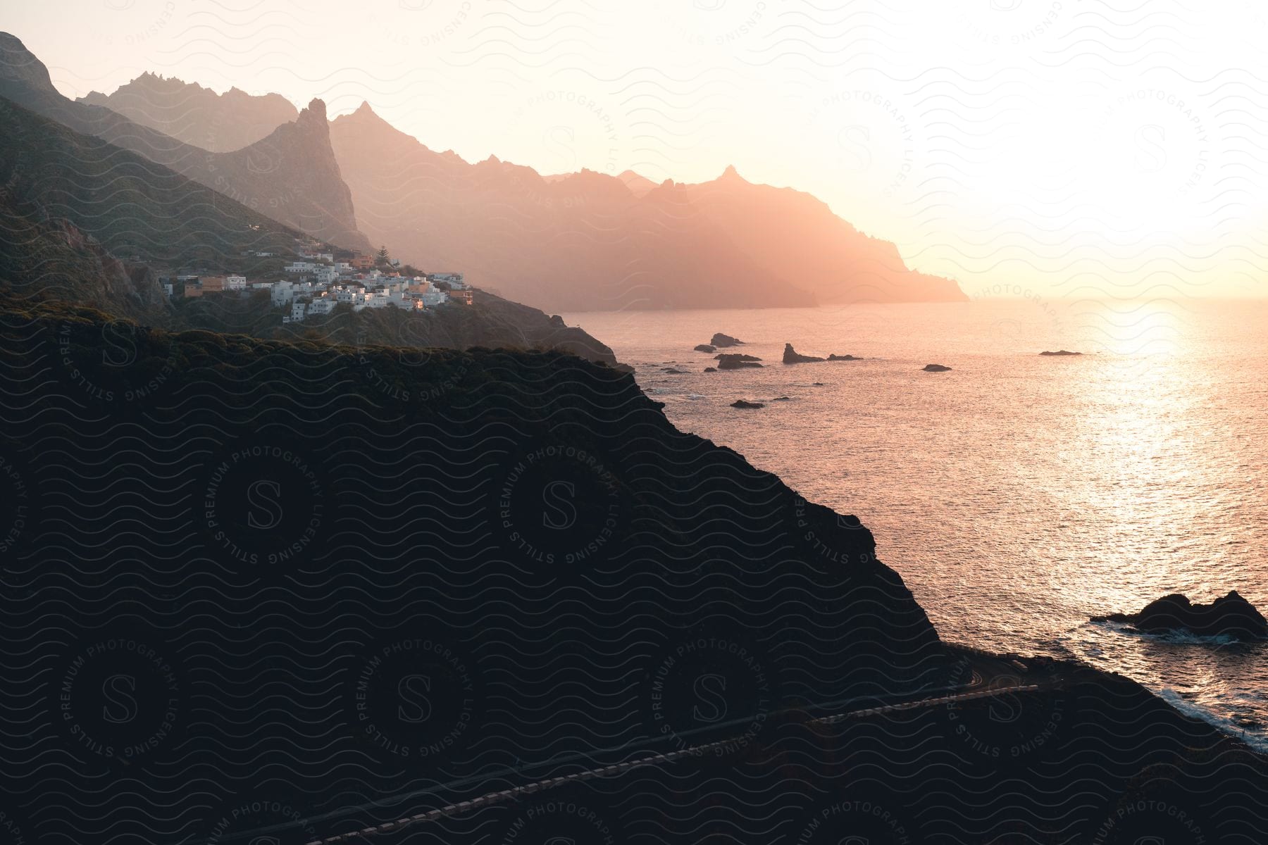 View of a mountainous coastline with houses and the sunset on the horizon.