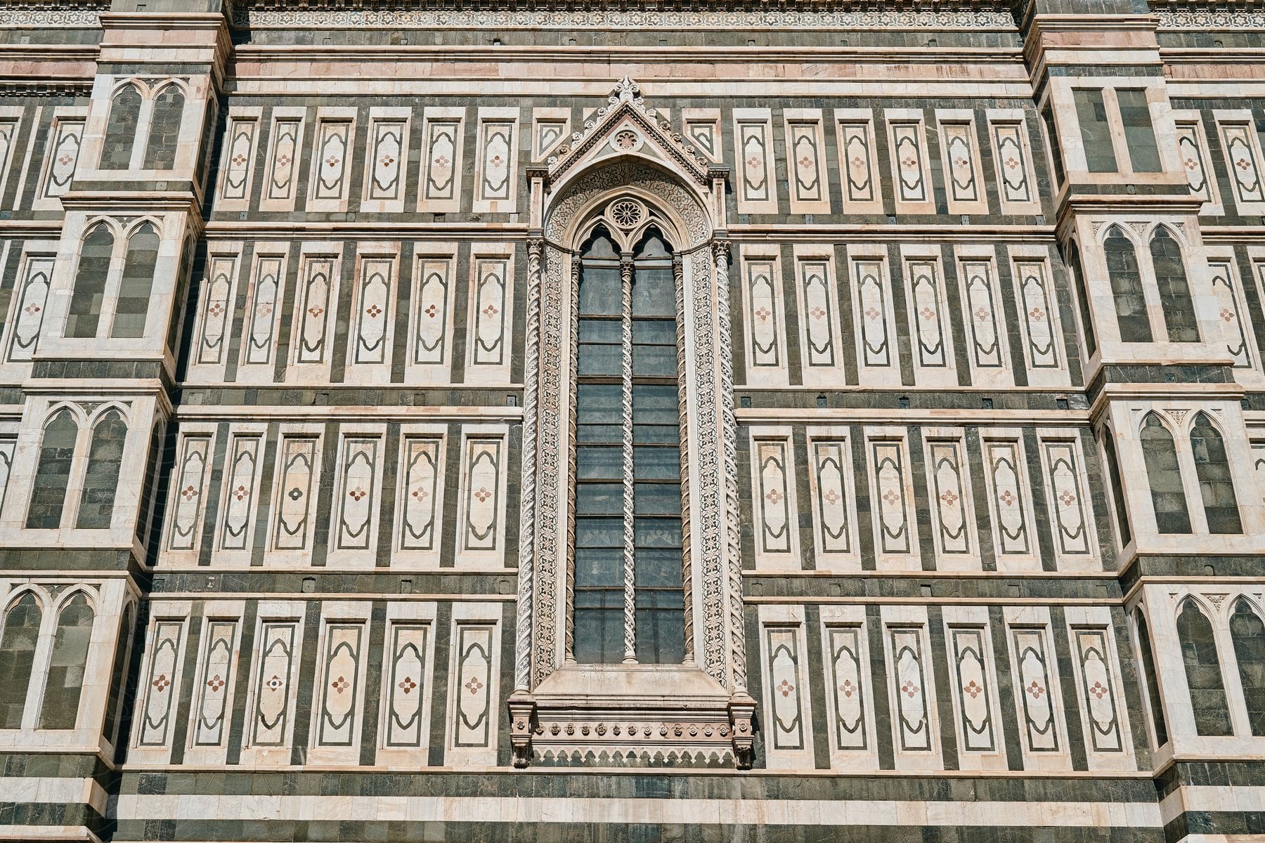 Repeating rectangular shapes separate large arched stained glasses window from columns of smaller windows on building.