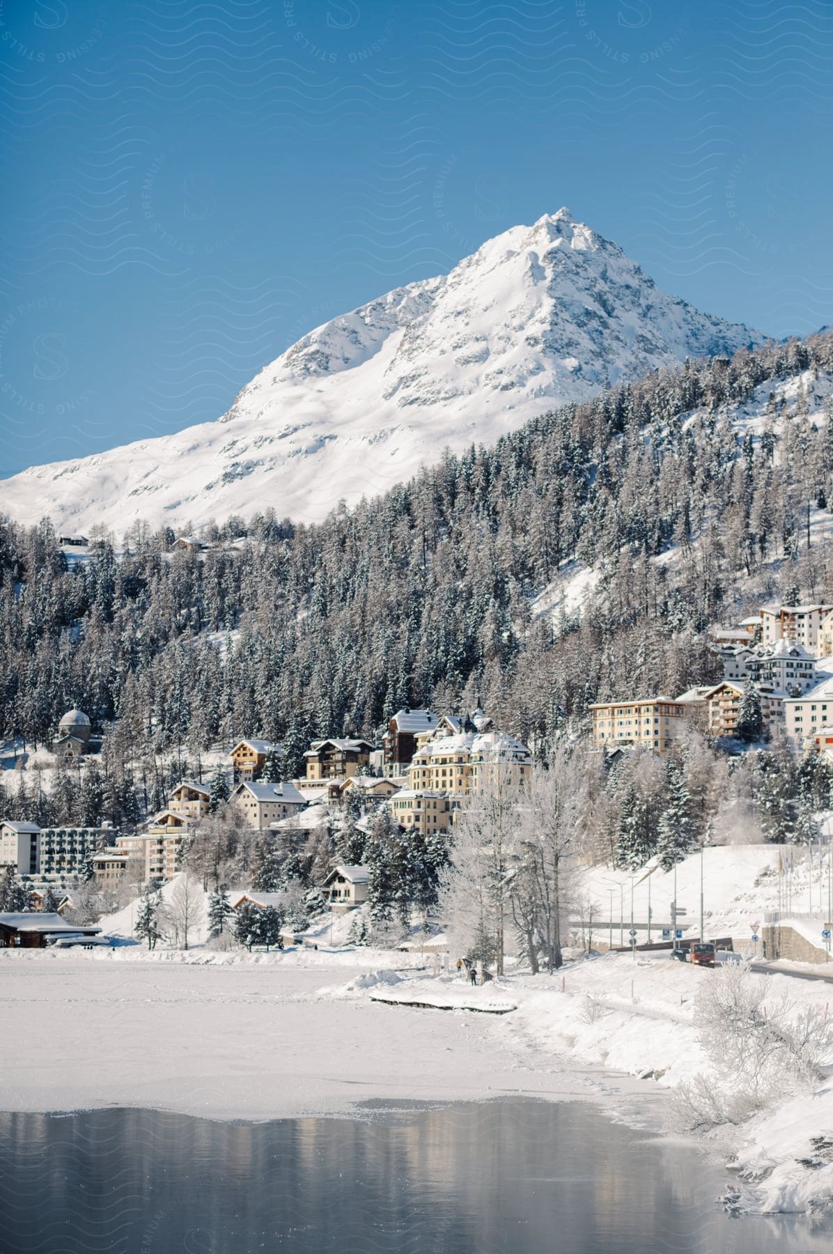 A majestic snow-capped peak towers over a frozen lake, with a cozy town nestled among snow-laden trees in the foreground.