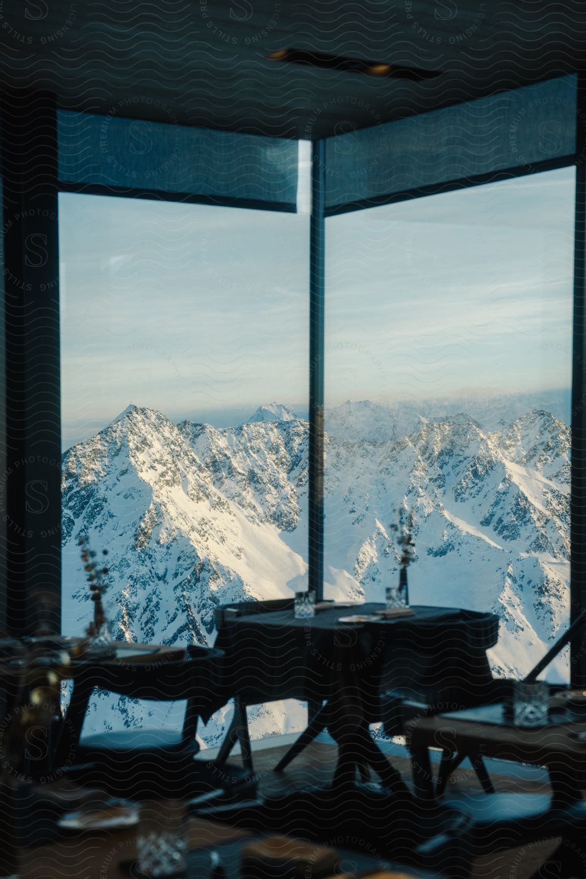 A view of an interior with restaurant tables and behind there is a glass window overlooking snowy mountains