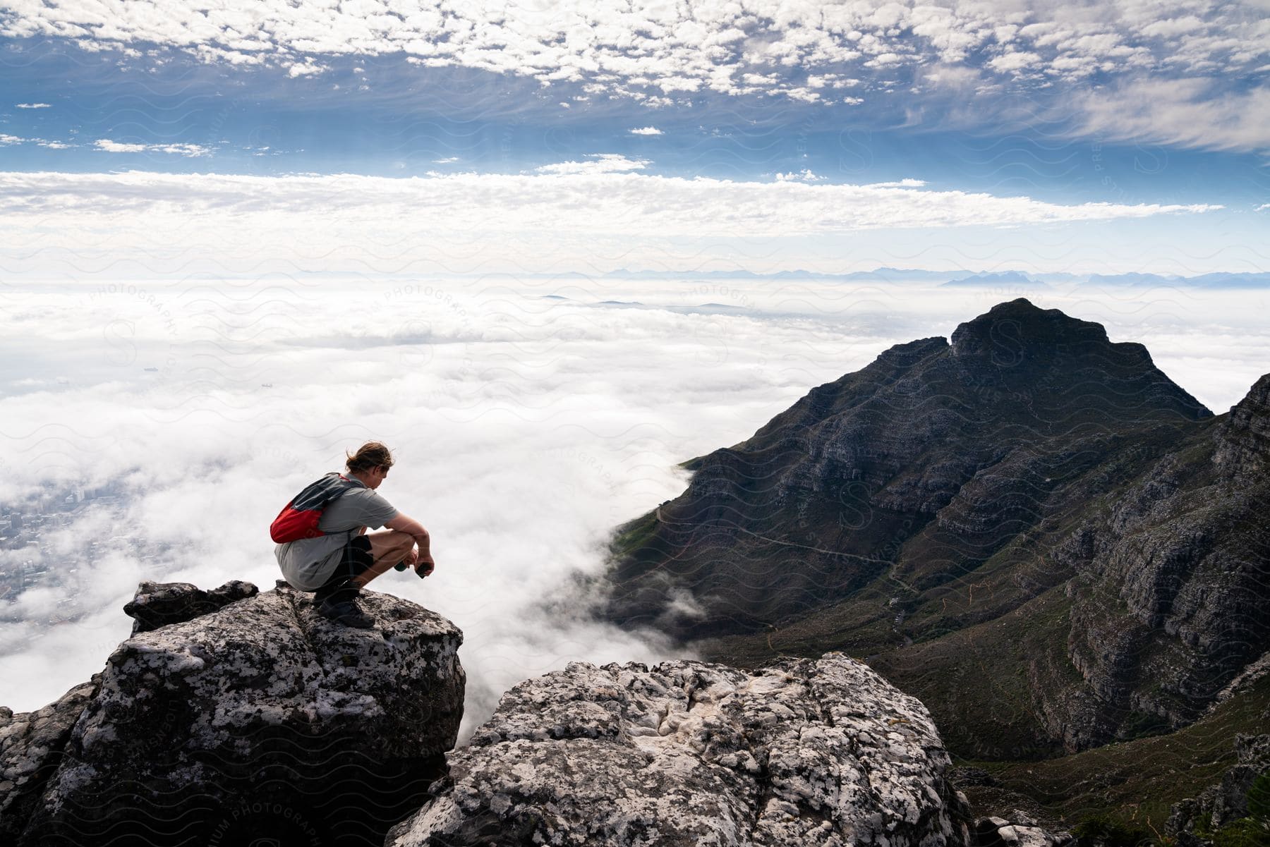 Hiker squatting down on a mountain rock high above the clouds