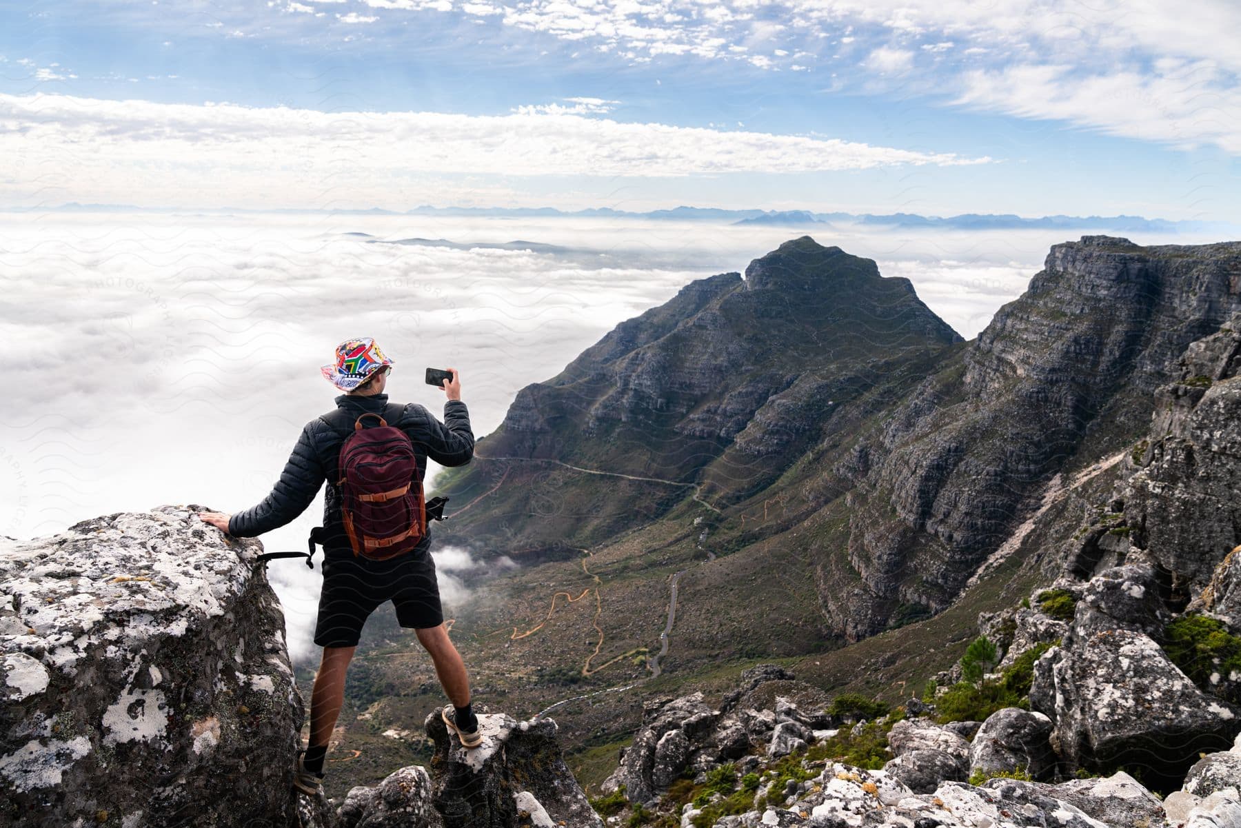 A triumphant hiker reaches the peak, a backpack on their back and a phone capturing the panorama of clouds swallowing the mountains below.