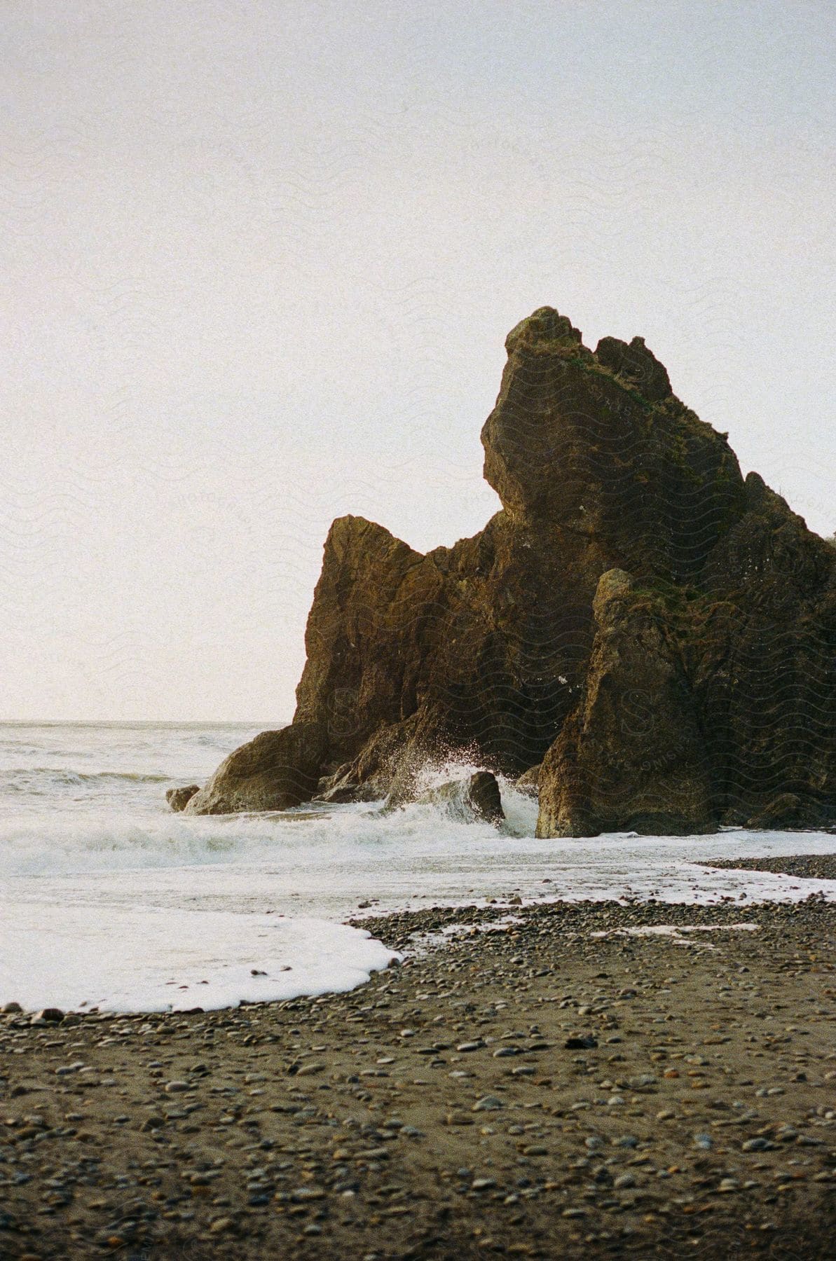 Jagged coastal rock beside the ocean and a rocky beach on a clouded day.