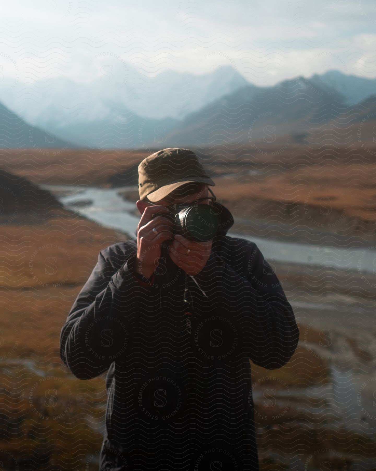 A person holding a camera taking photos while standing in front of a river and mountains.