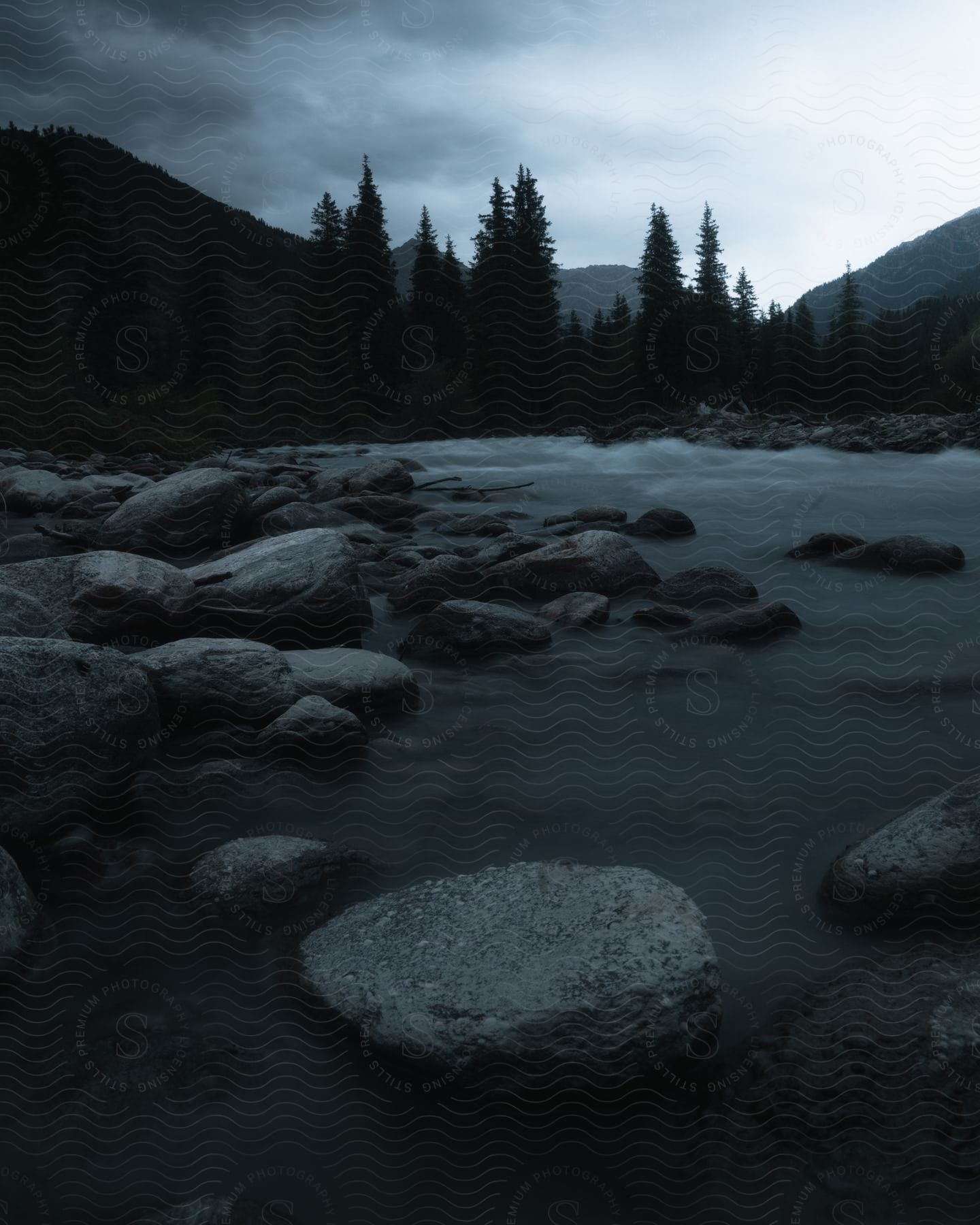 A lake filled with rocks is surrounded by trees on a cloudy evening.