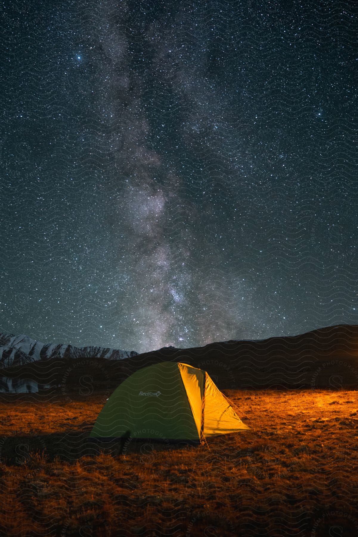 Landscape of a tent in a field with mountains around and a starry sky