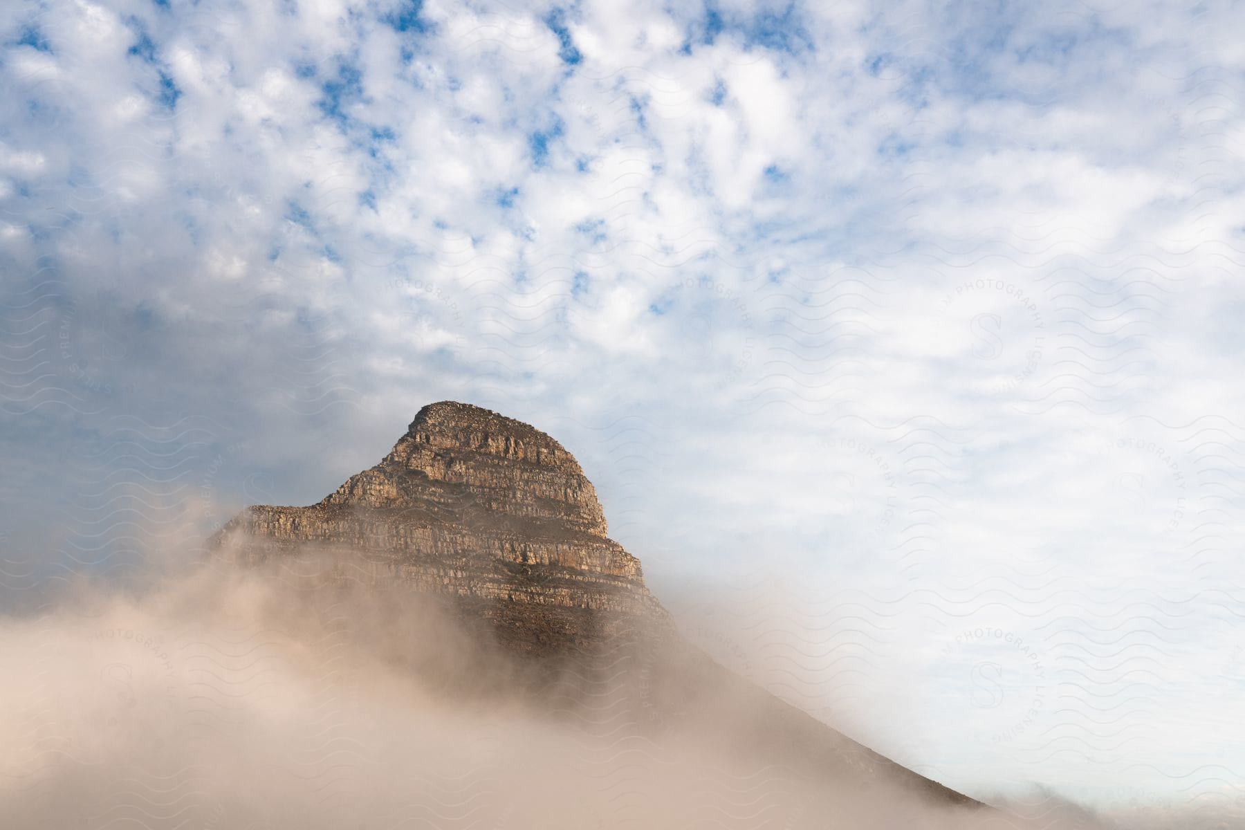 A majestic mountain emerges from a sea of mist under a sky dotted with clouds.