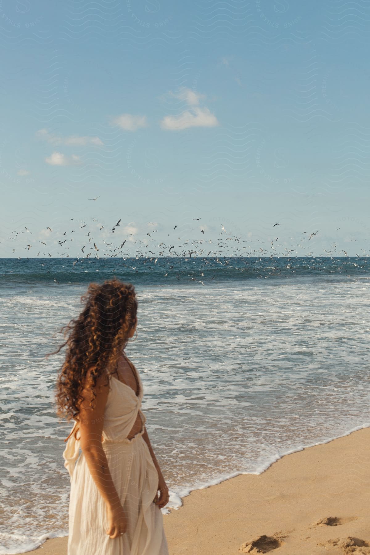 A person standing on the shore of a beach with clear sand and the sea in the background.