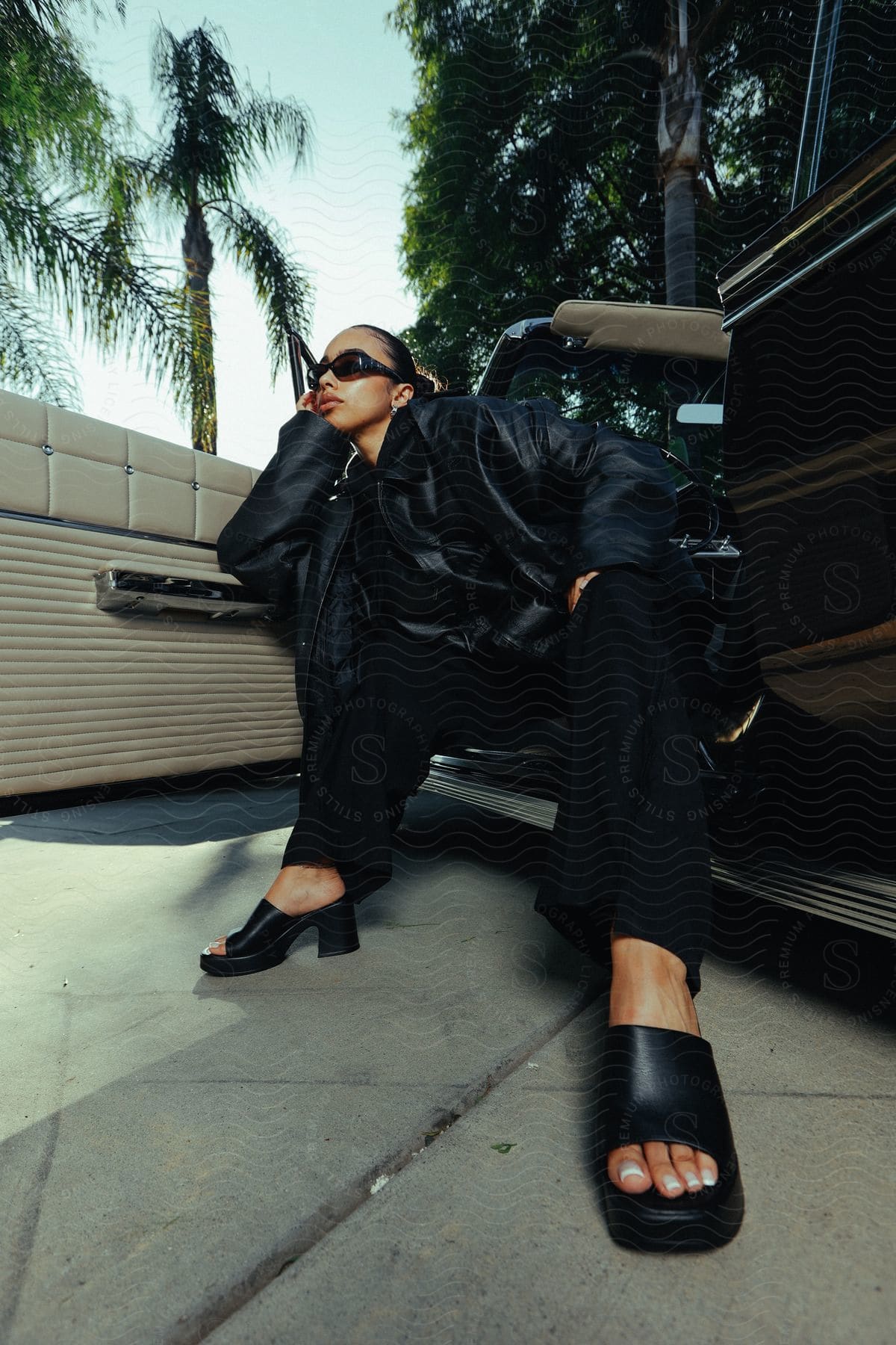 A woman posing and sitting on the edge of her car