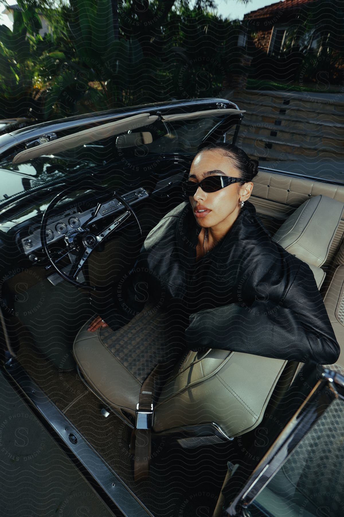 Woman wearing sunglasses and a black jacket sits in an open-top car