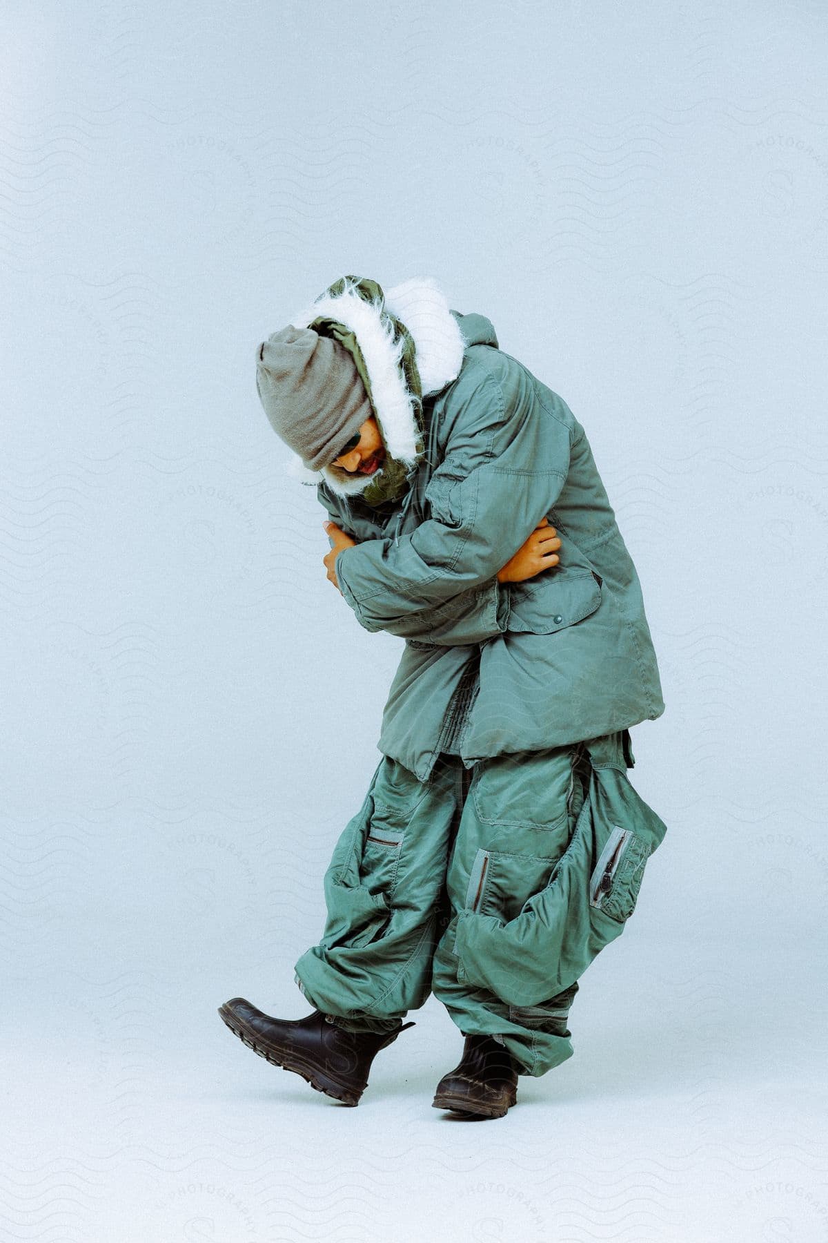 A man, donning a hat, sunglasses, a green winter coat, and pants, strikes a pose for the camera