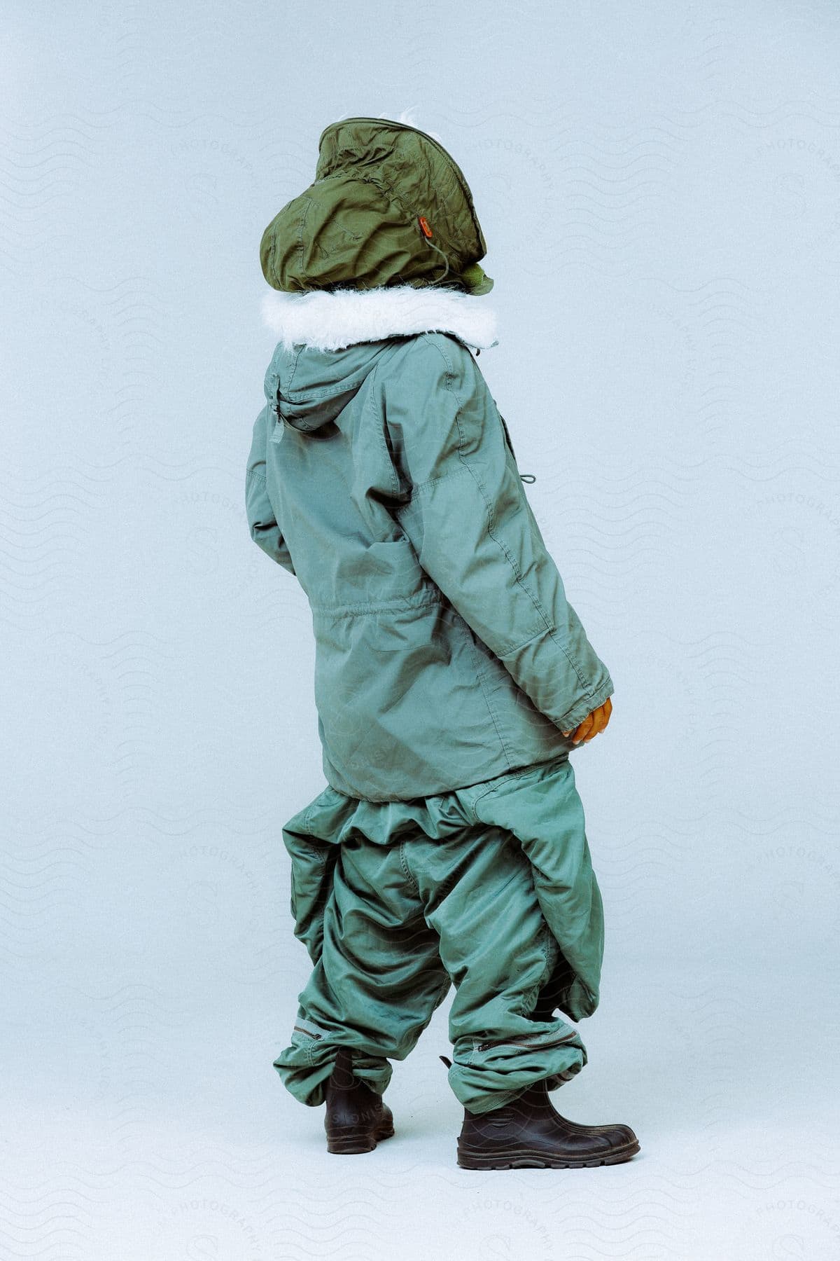 Child wearing a green Cold Weather Hood and a turquoise parka pants and a pair of black boots standing
