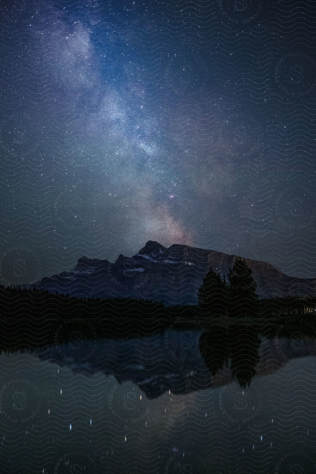 Landscape of a reflective lake with mountains in the background and a starry sky at night