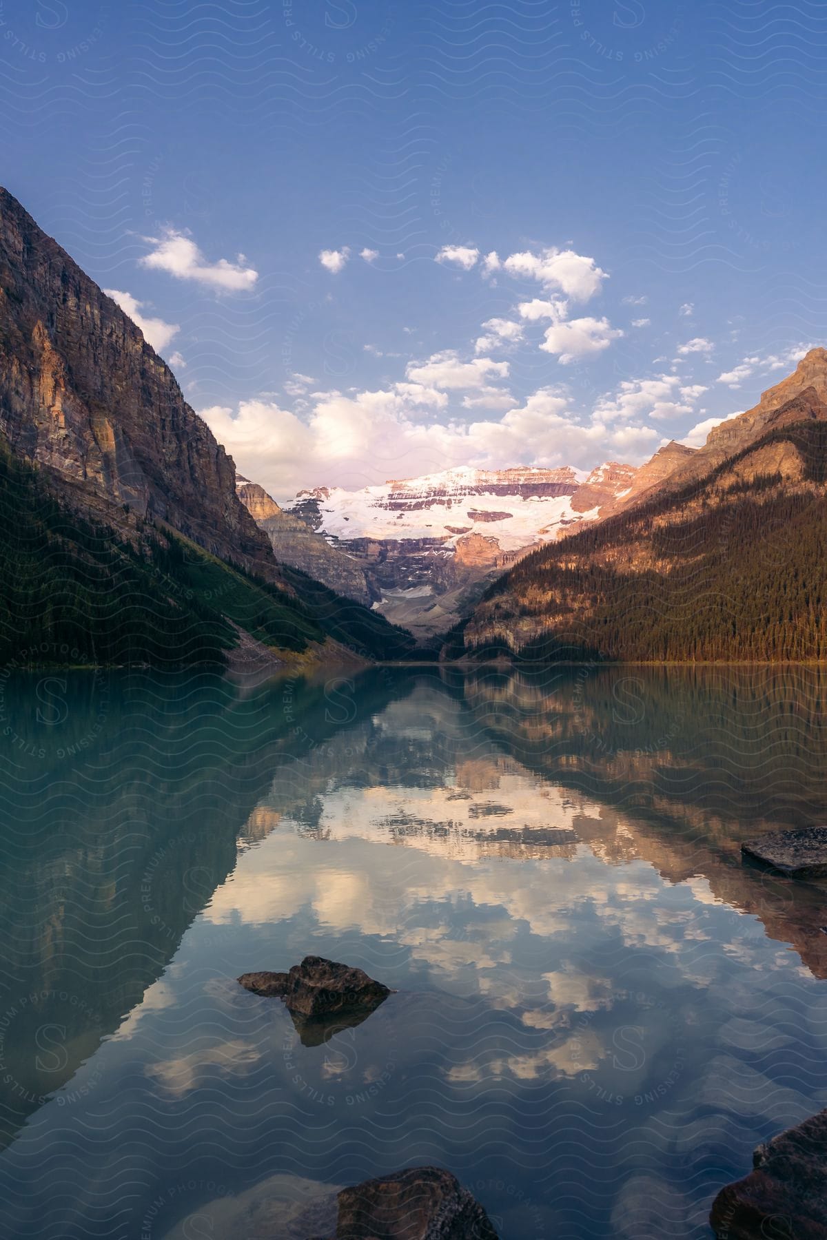 A snow-covered mountain is reflected in a still lake on a partly sunny day.