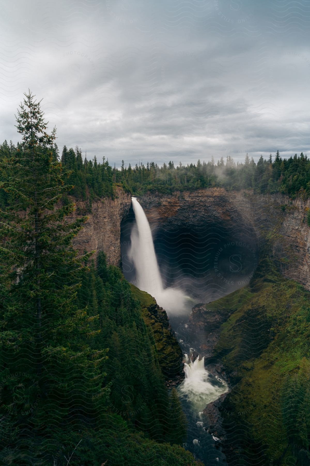 Waterfalls flow over a cliff in the forest under a cloudy sky