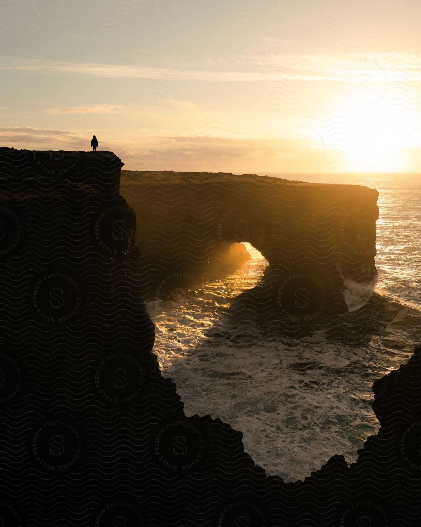 At sunrise, an individual stands on the Dyrhólaey Cliffs