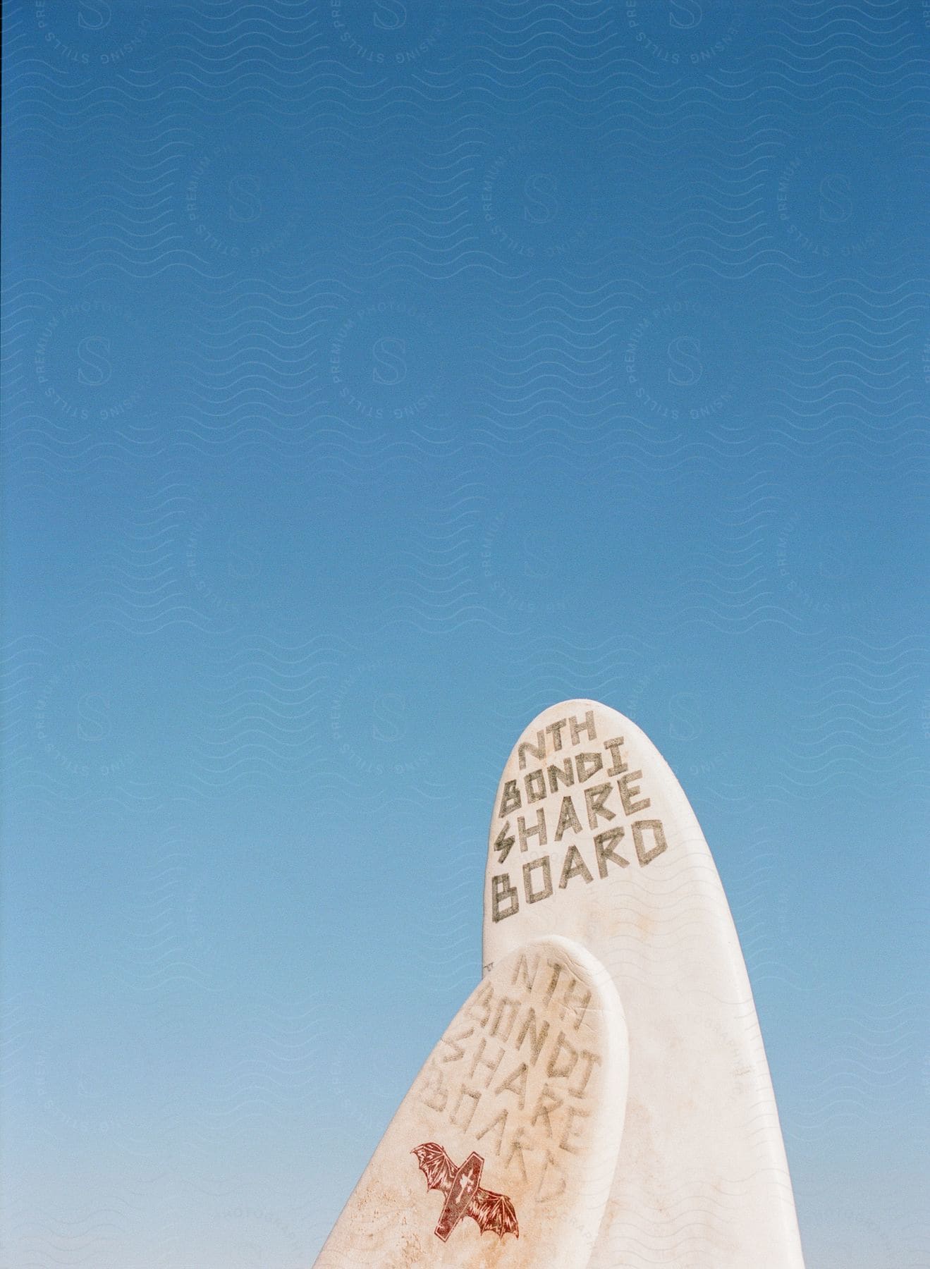 Close-up of a weathered surfboard against a clear blue sky, with text carved into it reading "Nth Bondi Share Board"