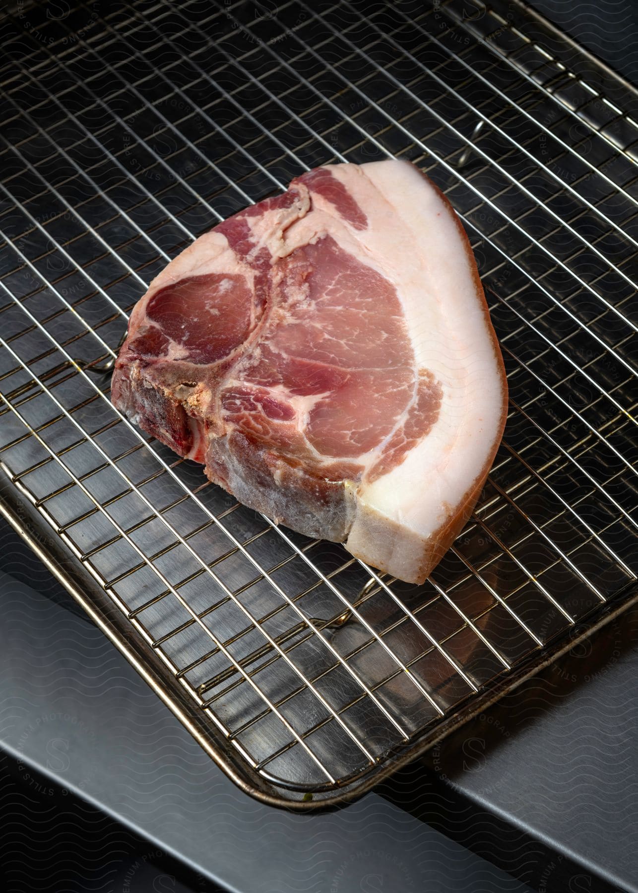 A thick, raw pork chop sits on top of a metal roasting pan.
