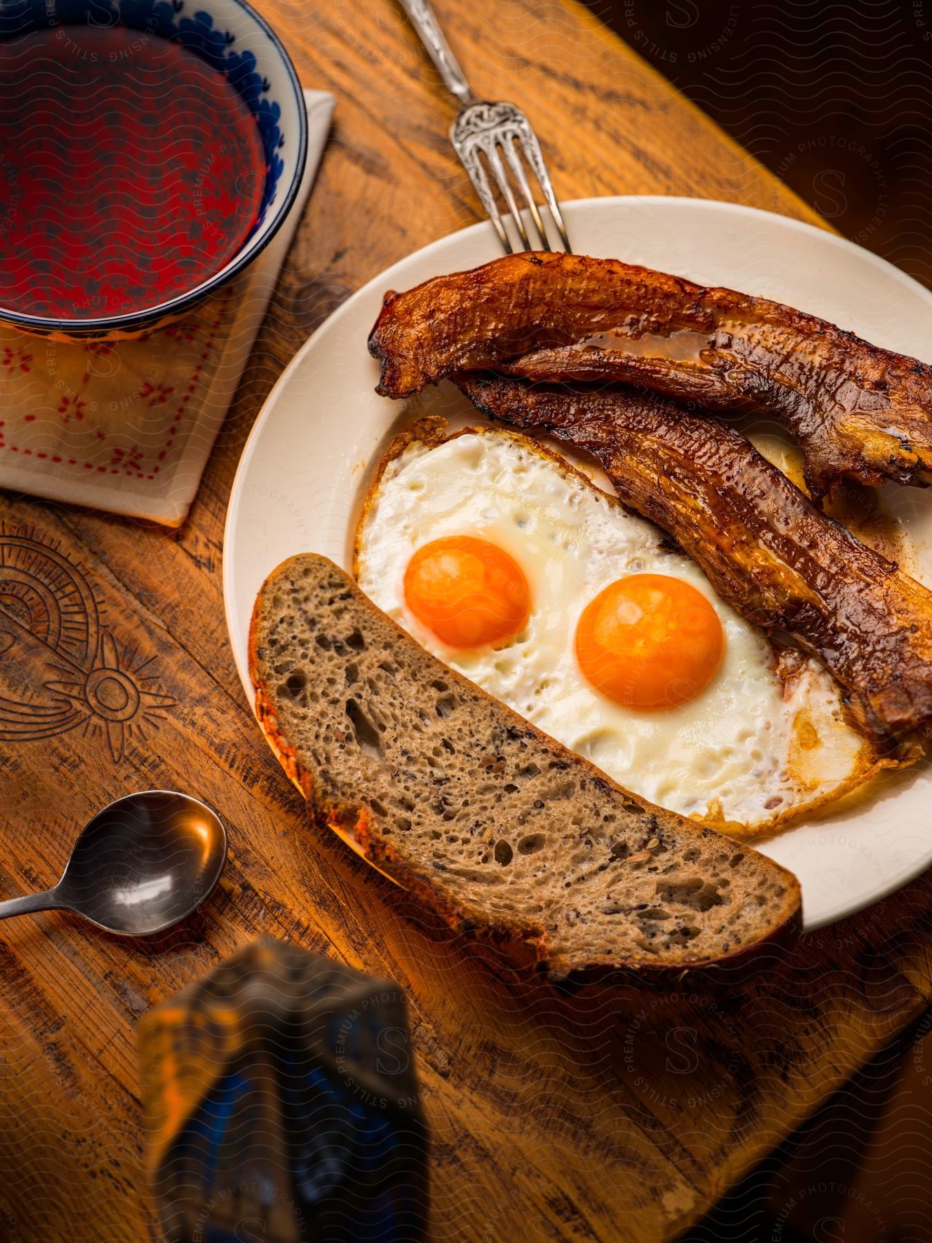 Bacon,  sunny side eggs, and rye toast with a cup of orange pekoe tea on a table