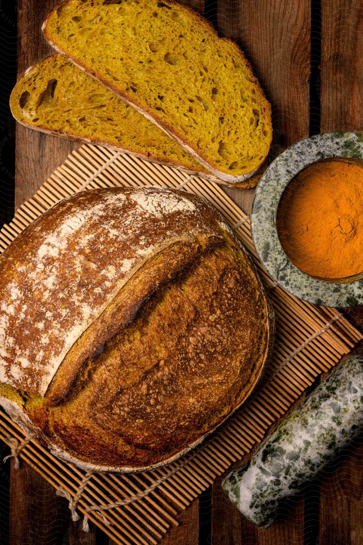 Artisanal loaf of bread display with slices on a wooden surface, alongside a bowl of orange spice.