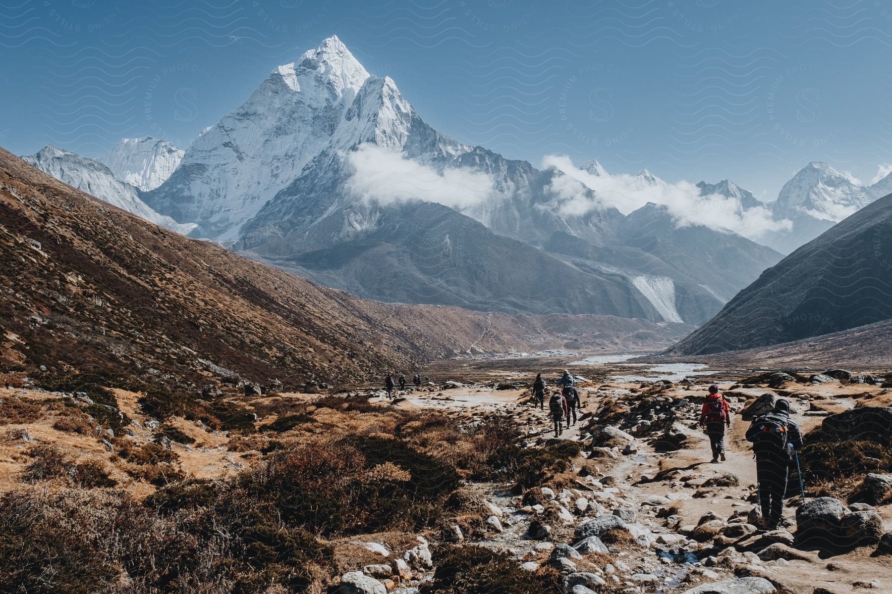 A group of people is hiking on a rocky path leading to an ice mountain during the daytime.