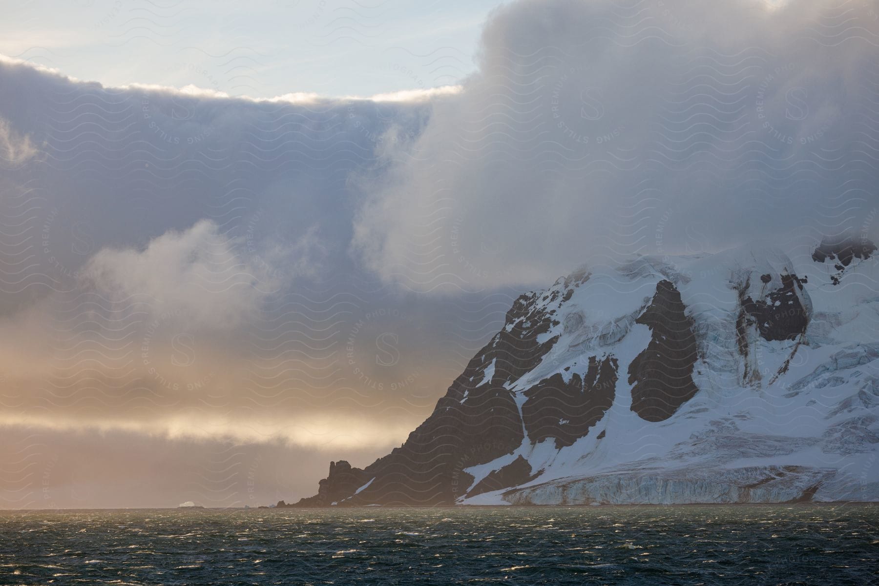 Clouds hang low over a snow covered mountain along the coast