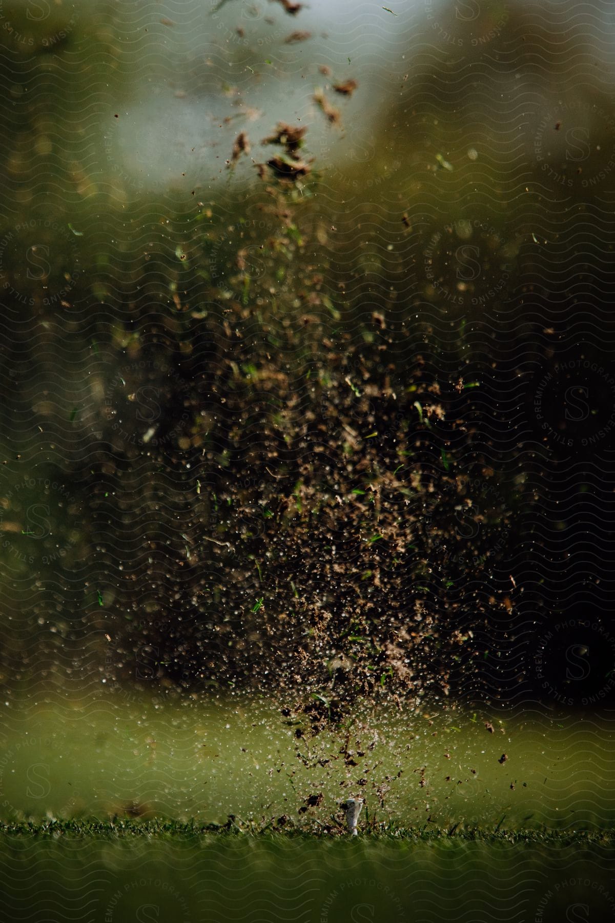 Dirt and grass debris flies into the air over golf tee after golf ball has been hit.