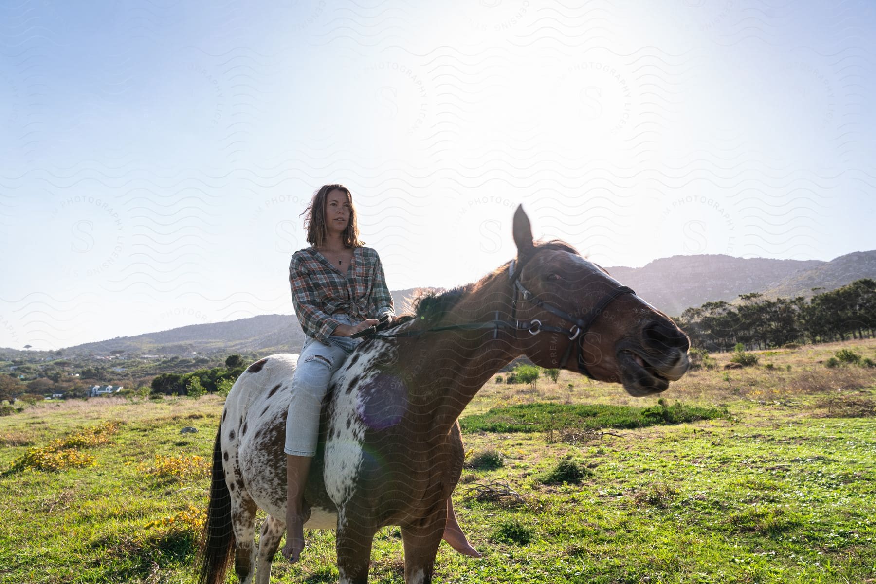 Barefoot woman riding a horse in a field with mountains in the background.